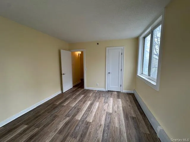 Unfurnished bedroom with baseboards, a textured ceiling, a baseboard radiator, and dark wood finished floors Unfurnished bedroom with baseboards, a textured ceiling, a baseboard radiator, and dark wood finished floors