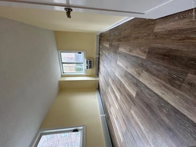 Unfurnished room with a wall mounted AC, a textured ceiling, baseboards, and wood finished floors Unfurnished room with a wall mounted AC, a textured ceiling, baseboards, and wood finished floors