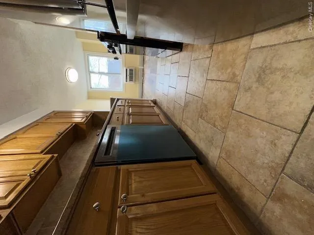 Kitchen featuring a wall mounted AC, baseboards, dark countertops, dishwashing machine, and stove Kitchen featuring a wall mounted AC, baseboards, dark countertops, dishwashing machine, and stove