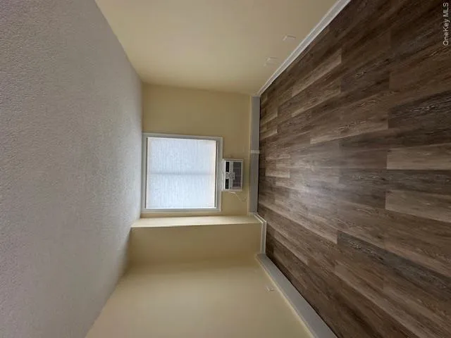 Empty room featuring a wall mounted air conditioner, a textured ceiling, baseboards, and dark wood finished floors Empty room featuring a wall mounted air conditioner, a textured ceiling, baseboards, and dark wood finished floors