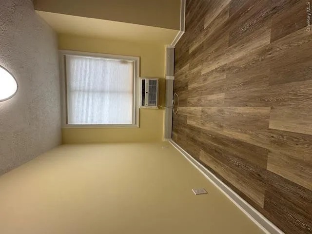 Empty room with a textured ceiling, a wall mounted air conditioner, baseboards, and dark wood-style flooring Empty room with a textured ceiling, a wall mounted air conditioner, baseboards, and dark wood-style flooring