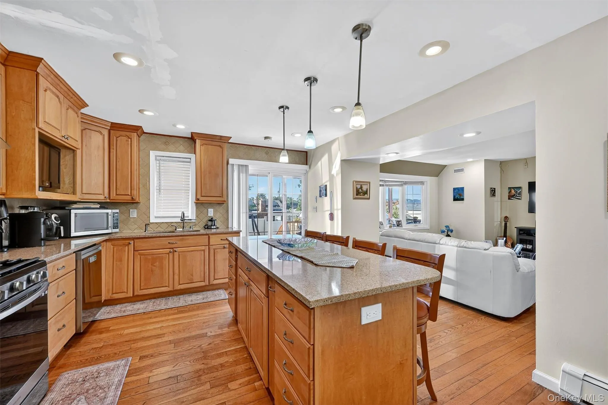 Kitchen featuring a kitchen bar, open floor plan, light stone counters, backsplash, and wood-style floors Kitchen featuring a kitchen bar, open floor plan, light stone counters, backsplash, and wood-style floors