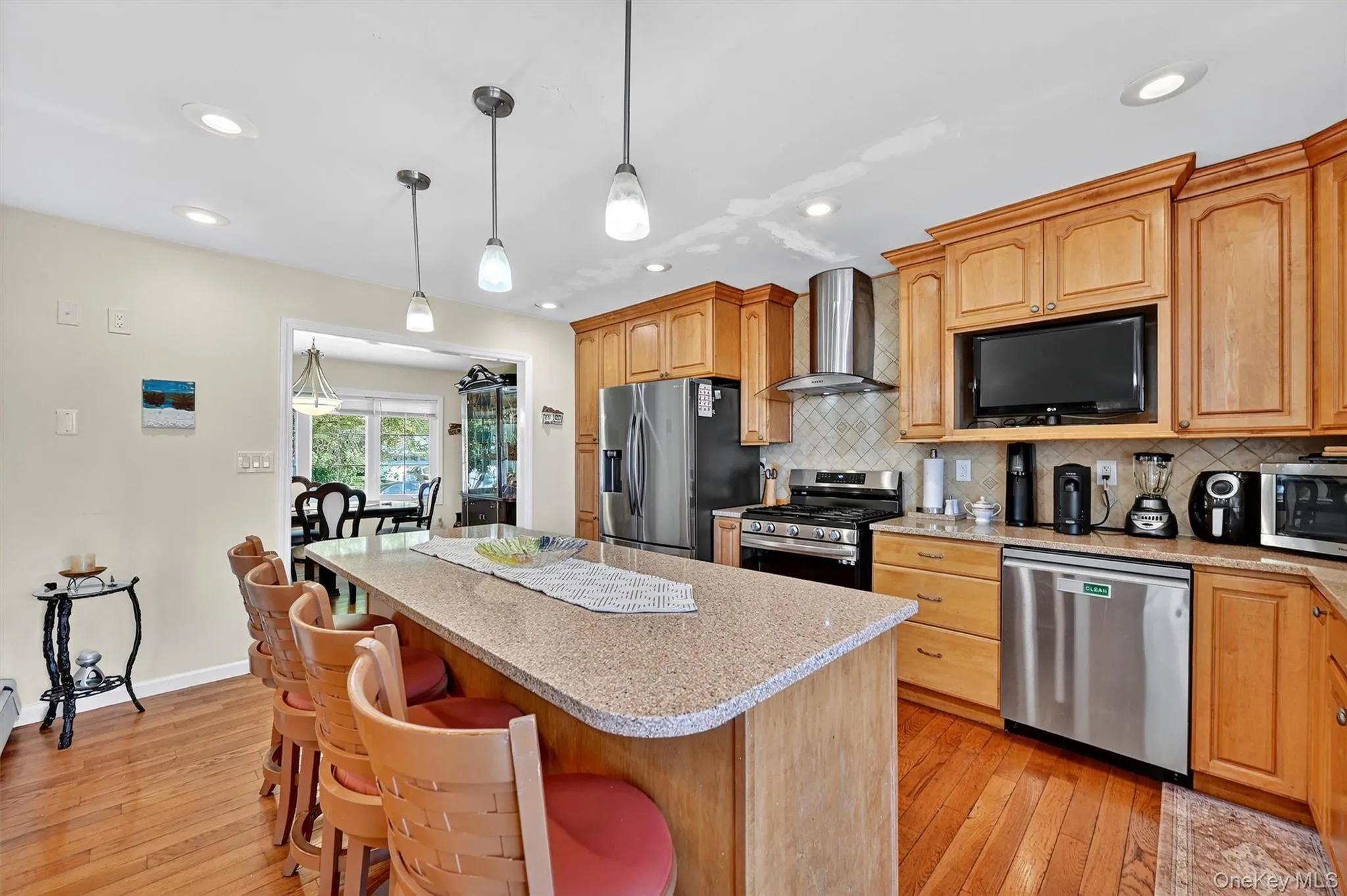 Kitchen with stainless steel appliances, decorative backsplash, wall chimney exhaust hood, pendant lighting, and light stone countertops Kitchen with stainless steel appliances, decorative backsplash, wall chimney exhaust hood, pendant lighting, and light stone countertops