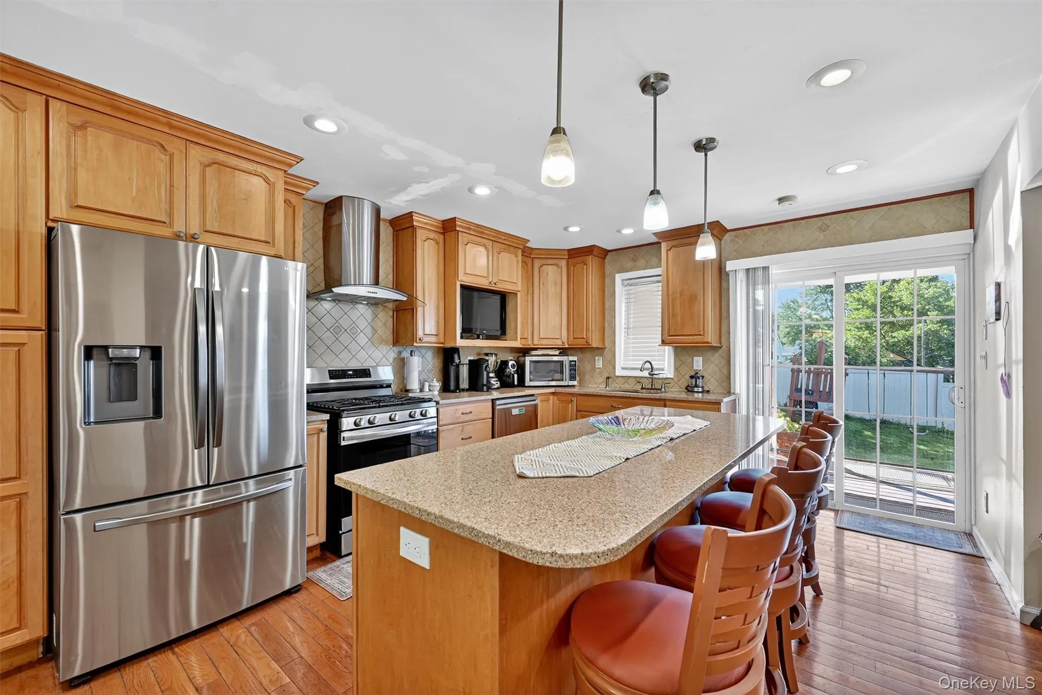 Kitchen featuring appliances with stainless steel finishes, decorative backsplash, light stone countertops, decorative light fixtures, and light wood finished floors Kitchen featuring appliances with stainless steel finishes, decorative backsplash, light stone countertops, decorative light fixtures, and light wood finished floors