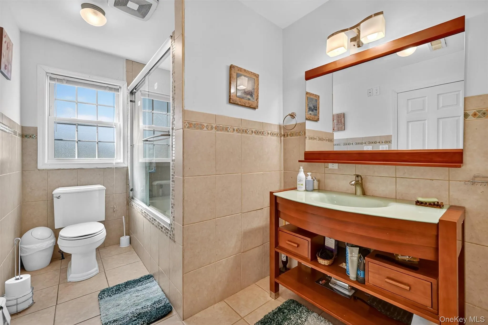 Bathroom featuring tile walls, tiled shower / bath, tile patterned flooring, wainscoting, and vanity Bathroom featuring tile walls, tiled shower / bath, tile patterned flooring, wainscoting, and vanity