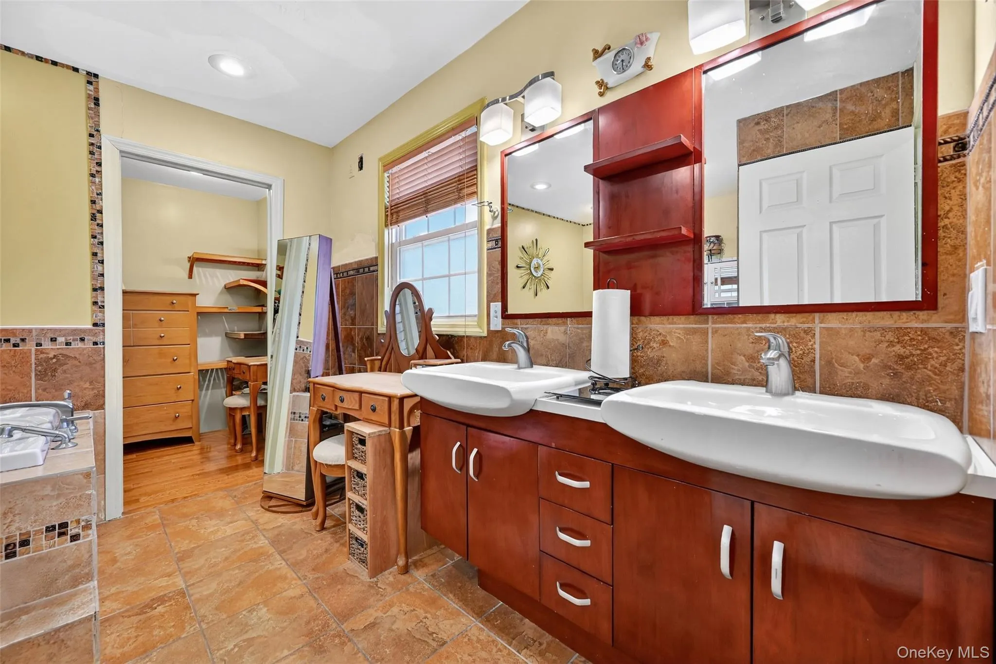 Full bath featuring tile walls, double vanity, wainscoting, a walk in closet, and a bath Full bath featuring tile walls, double vanity, wainscoting, a walk in closet, and a bath
