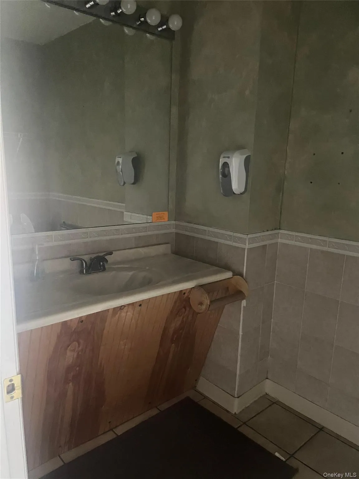 Bathroom vanity with a white sink, a mirror with exposed bulb lighting, and tiled walls Bathroom vanity with a white sink, a mirror with exposed bulb lighting, and tiled walls