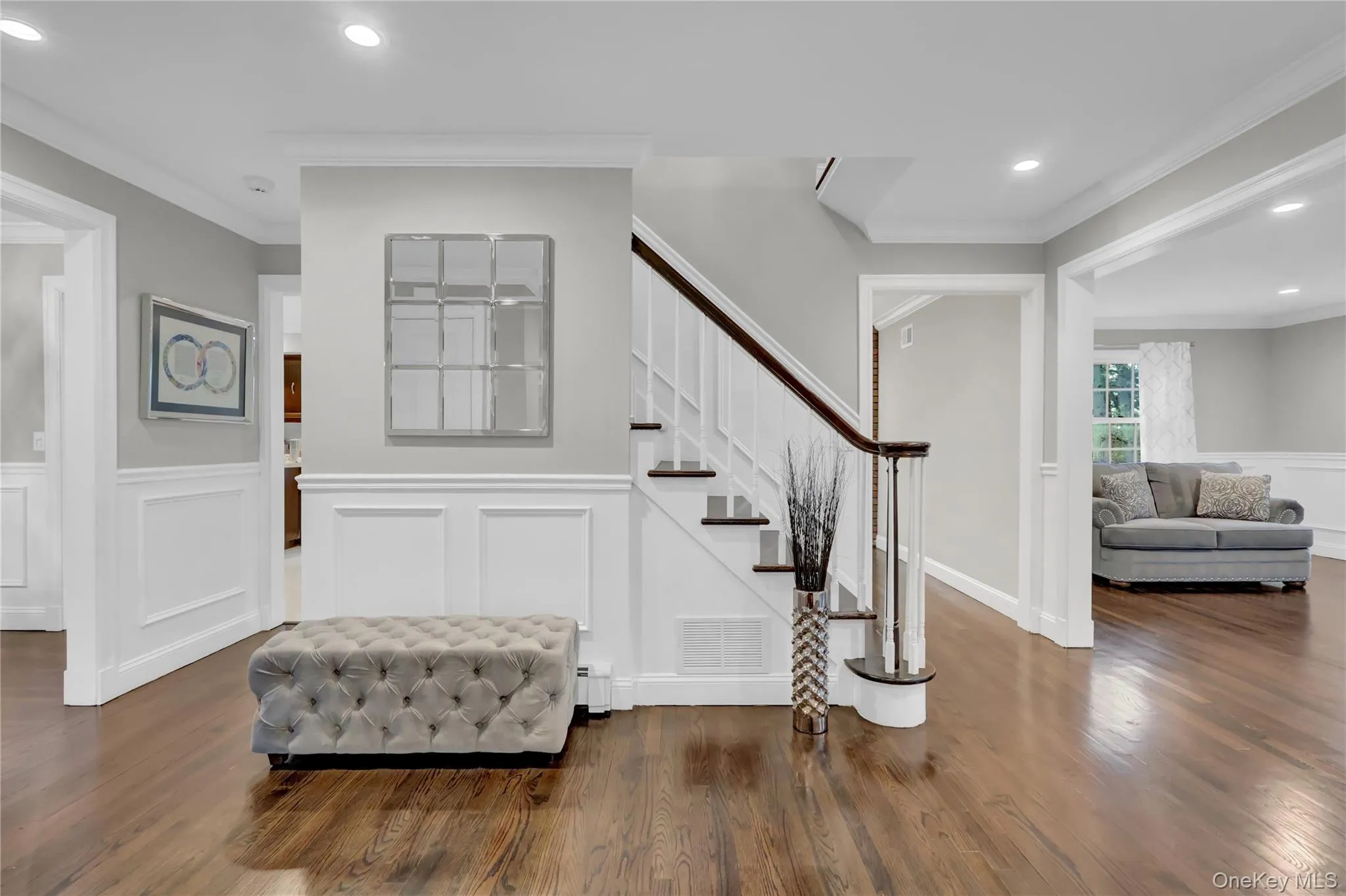 Hardwood flooring throughout the entry, staircase with white risers and dark wood handrail, recessed lighting, and crisp white wainscoting Hardwood flooring throughout the entry, staircase with white risers and dark wood handrail, recessed lighting, and crisp white wainscoting