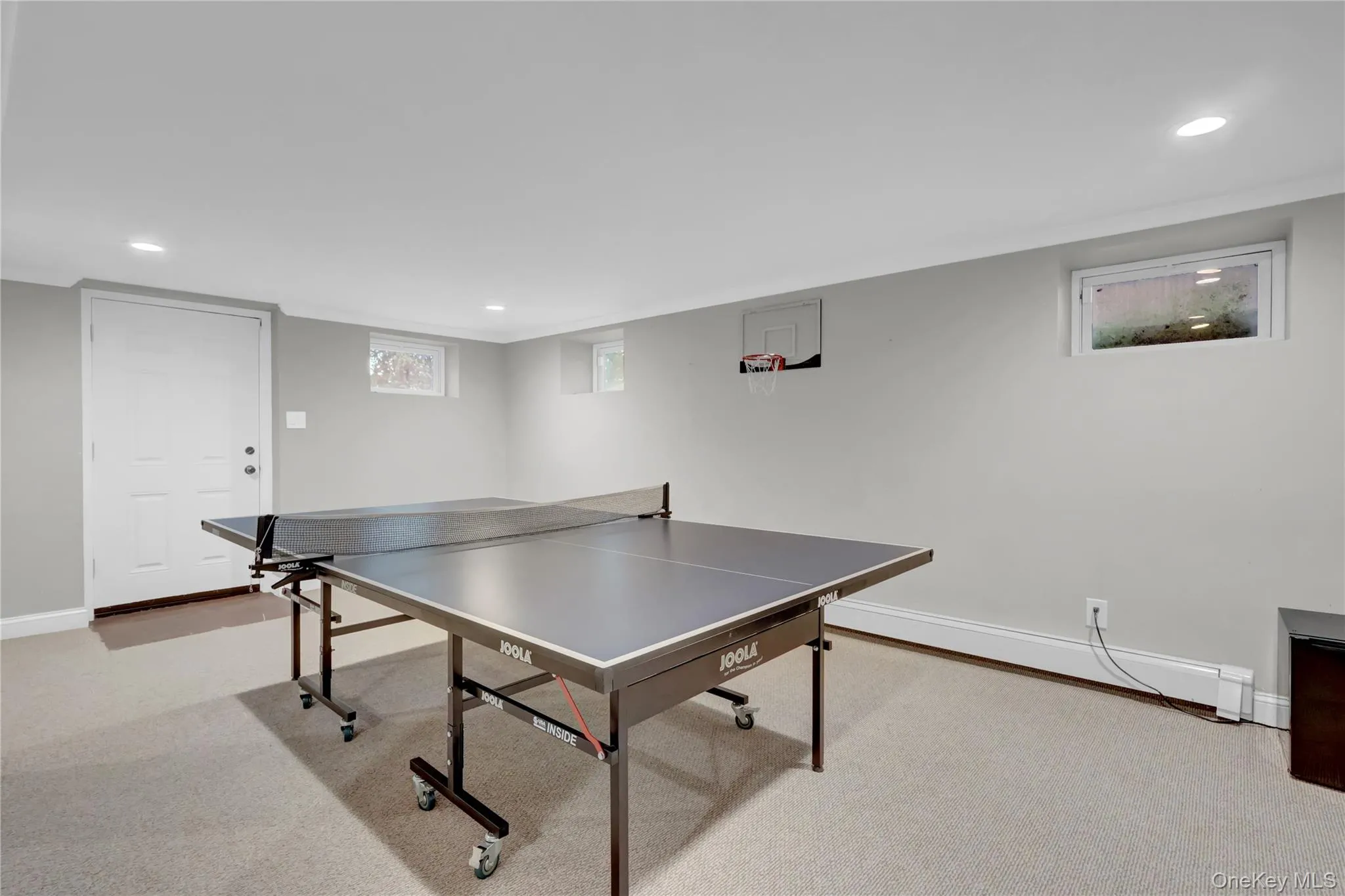 Versatile lower-level space featuring recessed lighting, light-toned carpeting, and a white egress door Versatile lower-level space featuring recessed lighting, light-toned carpeting, and a white egress door