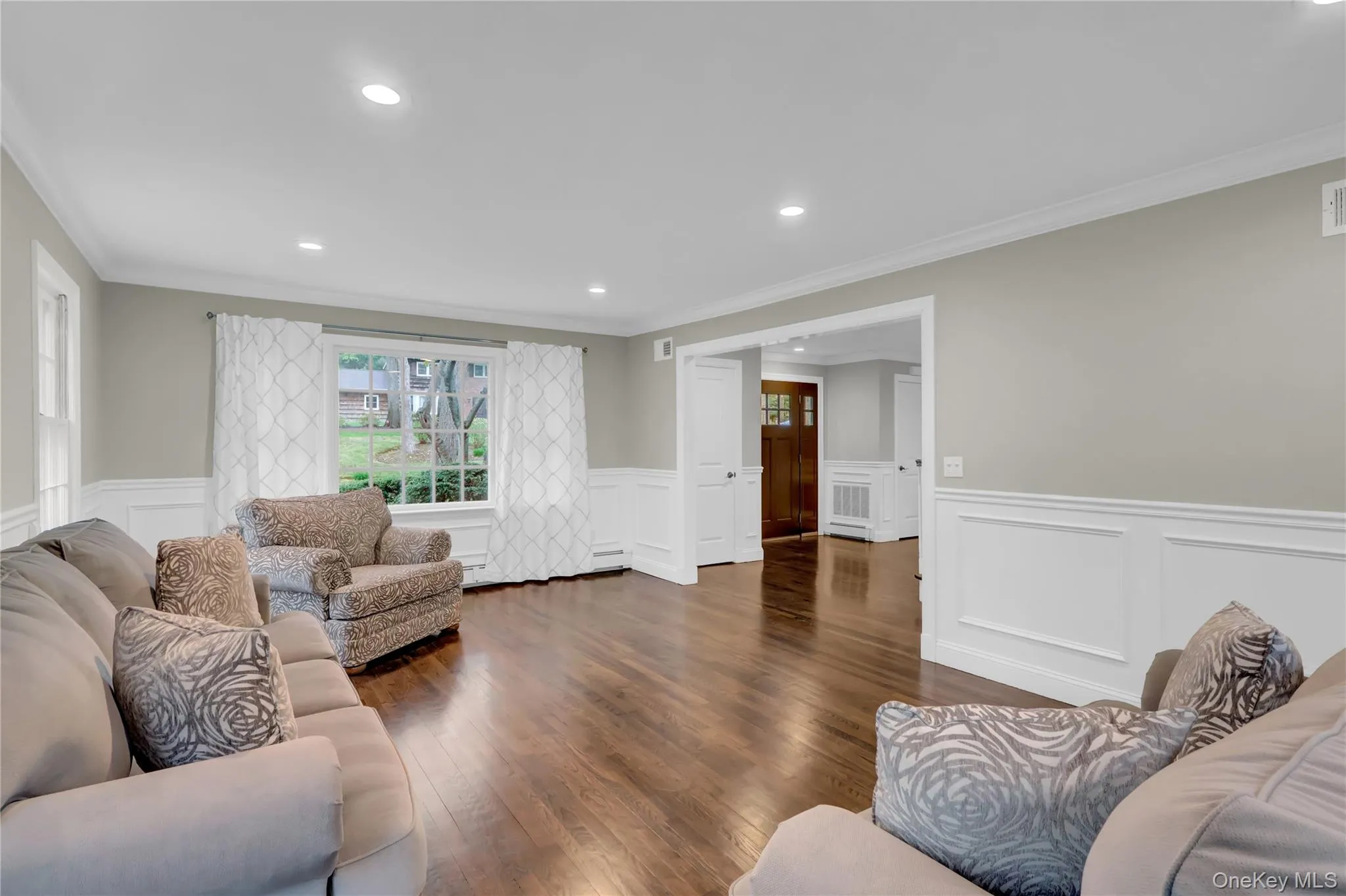 Spacious living area featuring polished wood-finish flooring, white wainscoting, and recessed lighting Spacious living area featuring polished wood-finish flooring, white wainscoting, and recessed lighting