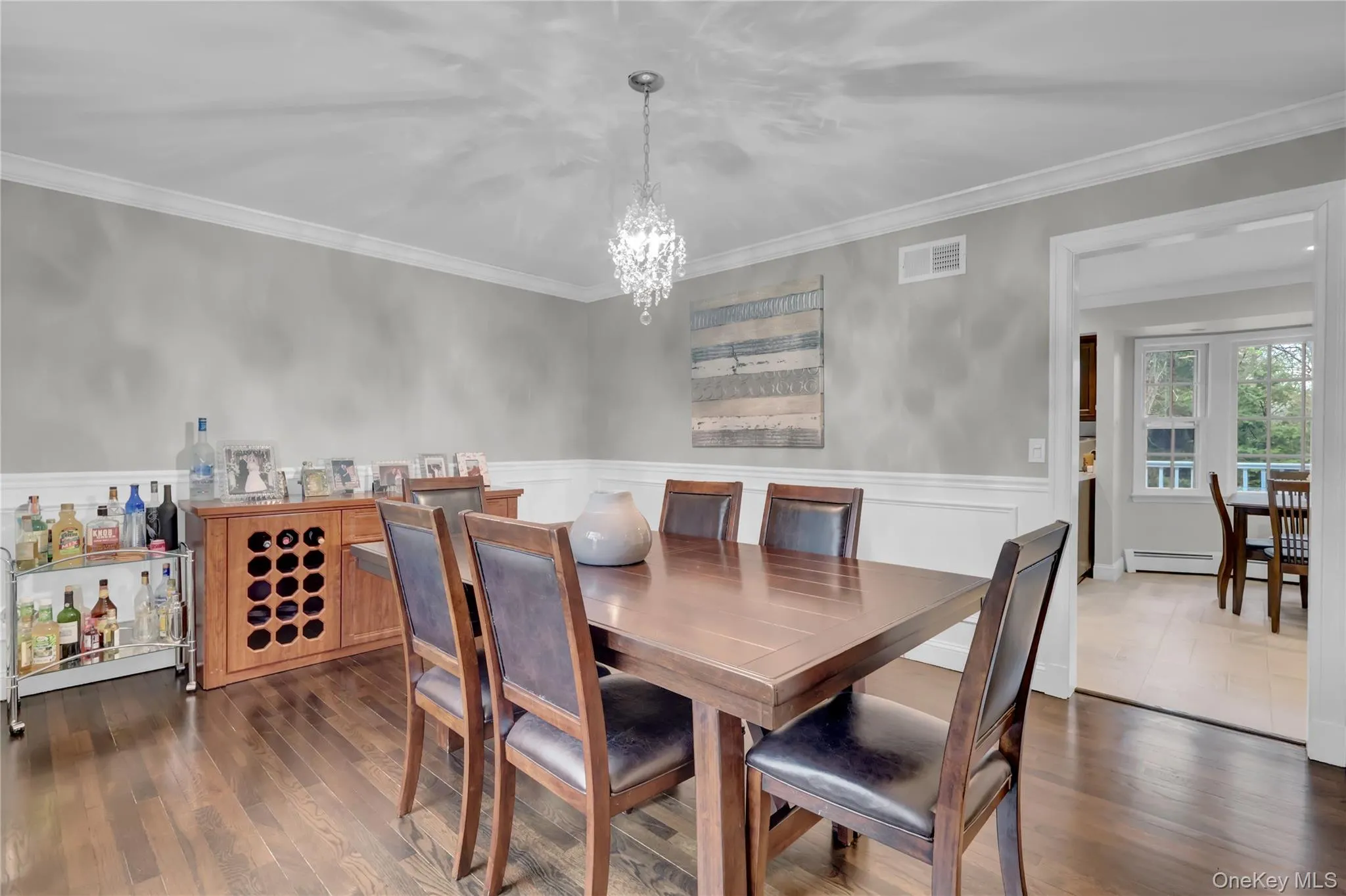 Formal dining space featuring wood-finish flooring, white crown molding, and wainscoting Formal dining space featuring wood-finish flooring, white crown molding, and wainscoting