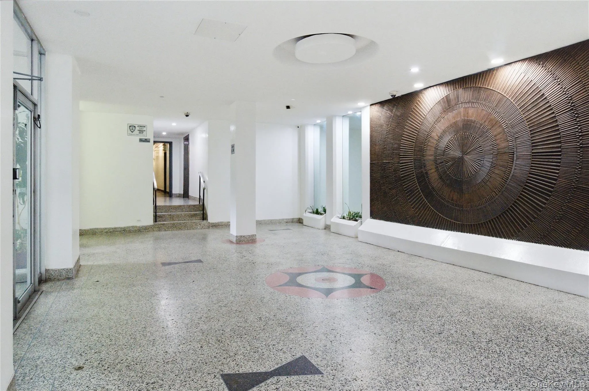 The building's entrance features a large decorative wall panel, recessed lighting, and a patterned floor The building's entrance features a large decorative wall panel, recessed lighting, and a patterned floor