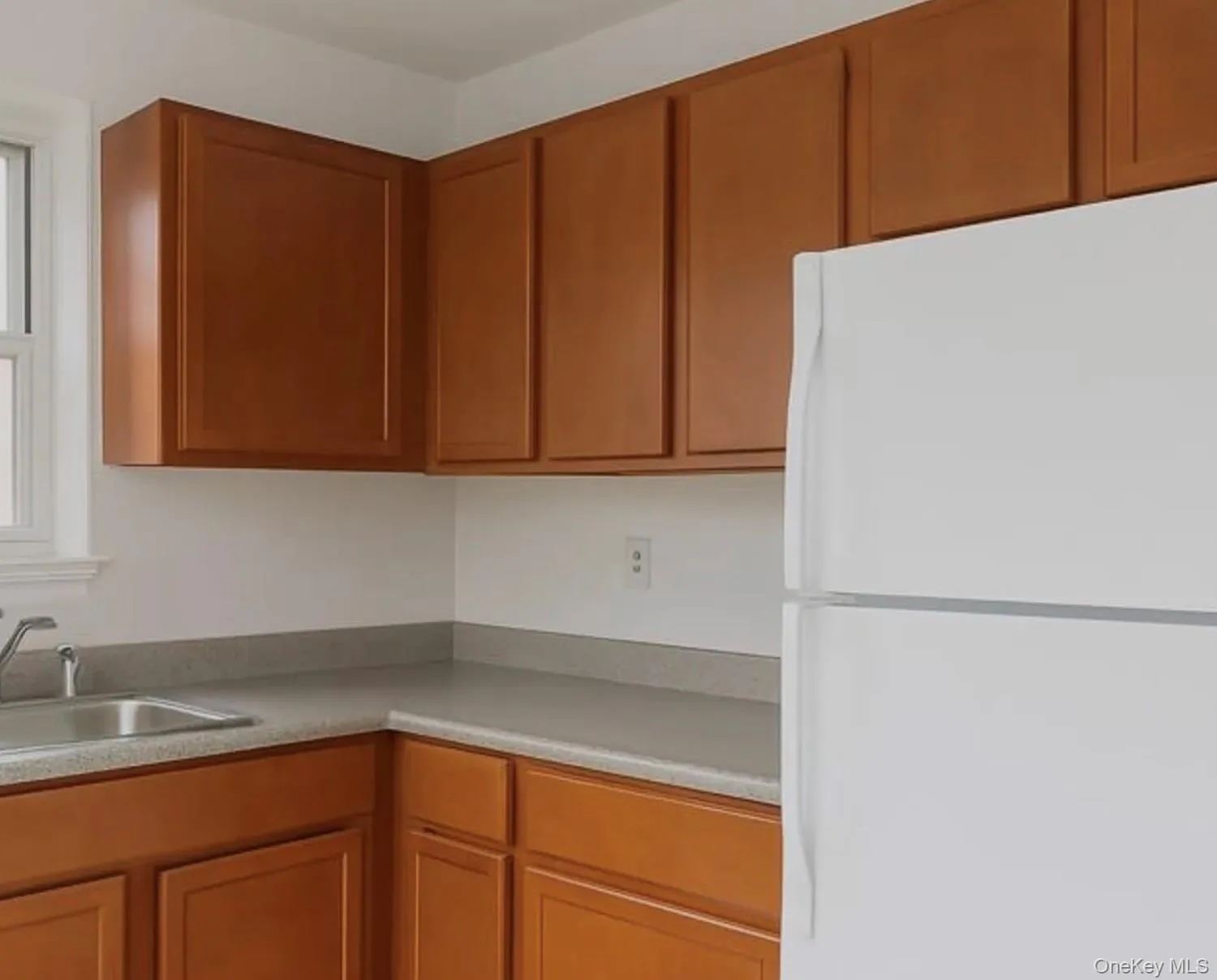 Kitchen featuring freestanding refrigerator, brown cabinets, and light countertops Kitchen featuring freestanding refrigerator, brown cabinets, and light countertops