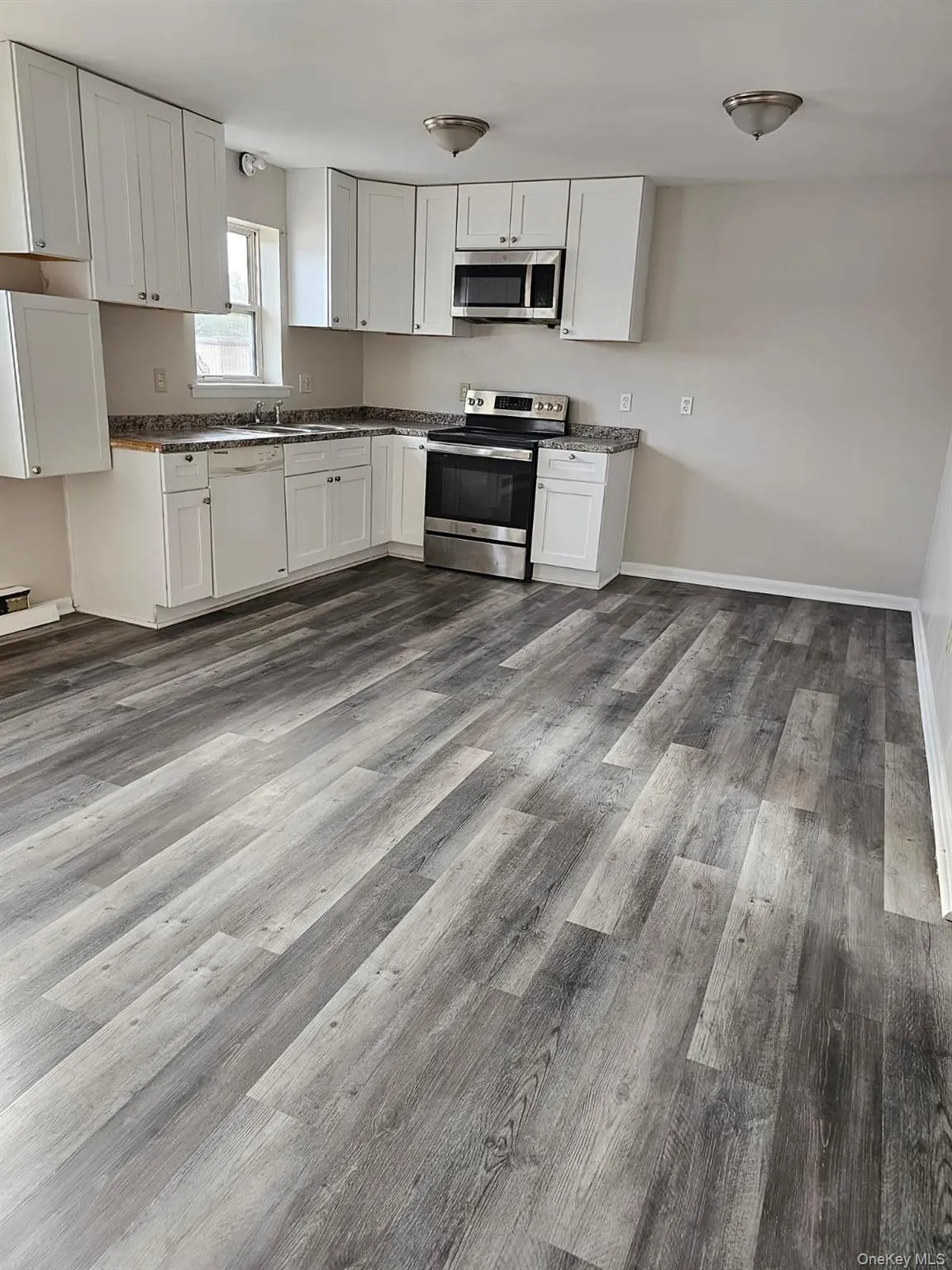 Kitchen featuring stainless steel appliances, a sink, dark countertops, dark wood-style flooring, and white cabinetry Kitchen featuring stainless steel appliances, a sink, dark countertops, dark wood-style flooring, and white cabinetry