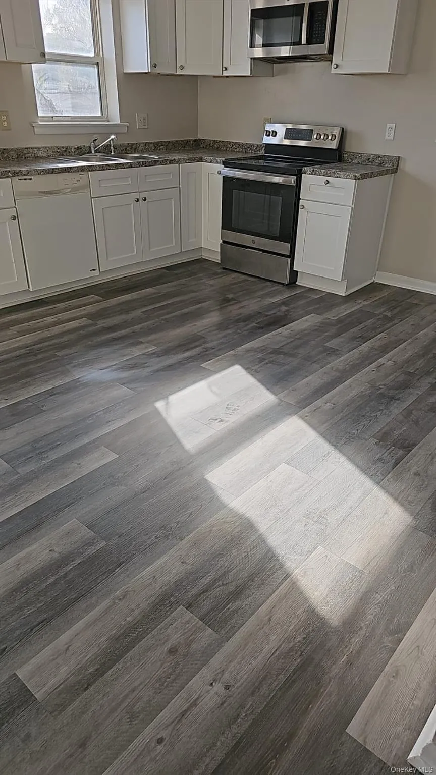 Kitchen featuring appliances with stainless steel finishes, dark wood-type flooring, white cabinetry, baseboards, and a sink Kitchen featuring appliances with stainless steel finishes, dark wood-type flooring, white cabinetry, baseboards, and a sink