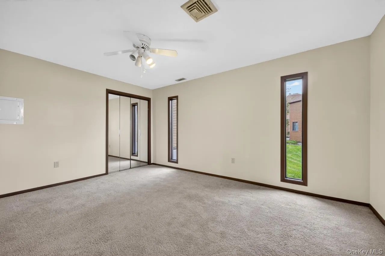 Carpeted room featuring a ceiling fan, two vertical windows with dark trim, and a mirrored closet door Carpeted room featuring a ceiling fan, two vertical windows with dark trim, and a mirrored closet door
