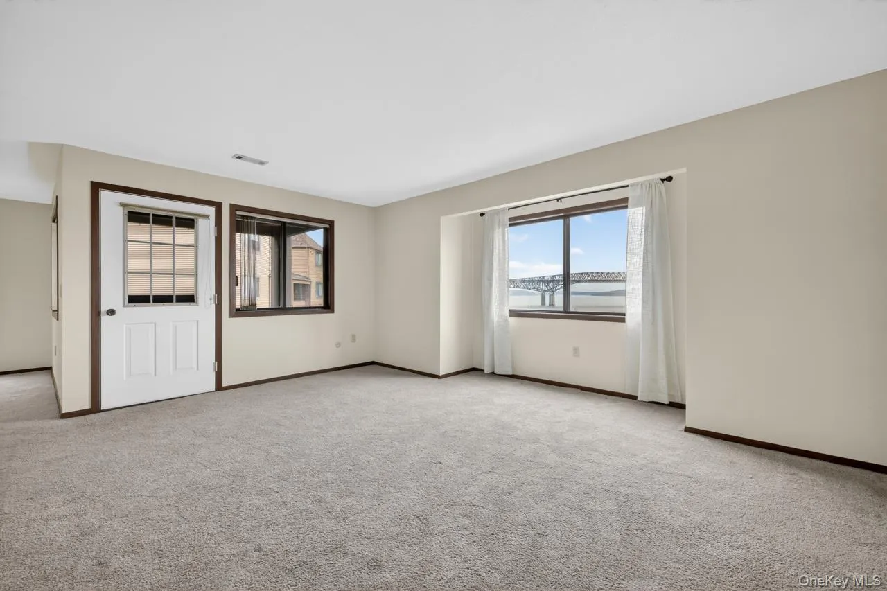 Carpeted room featuring light-toned walls, a white door with grid-patterned glass panels, and dark wood trim Carpeted room featuring light-toned walls, a white door with grid-patterned glass panels, and dark wood trim