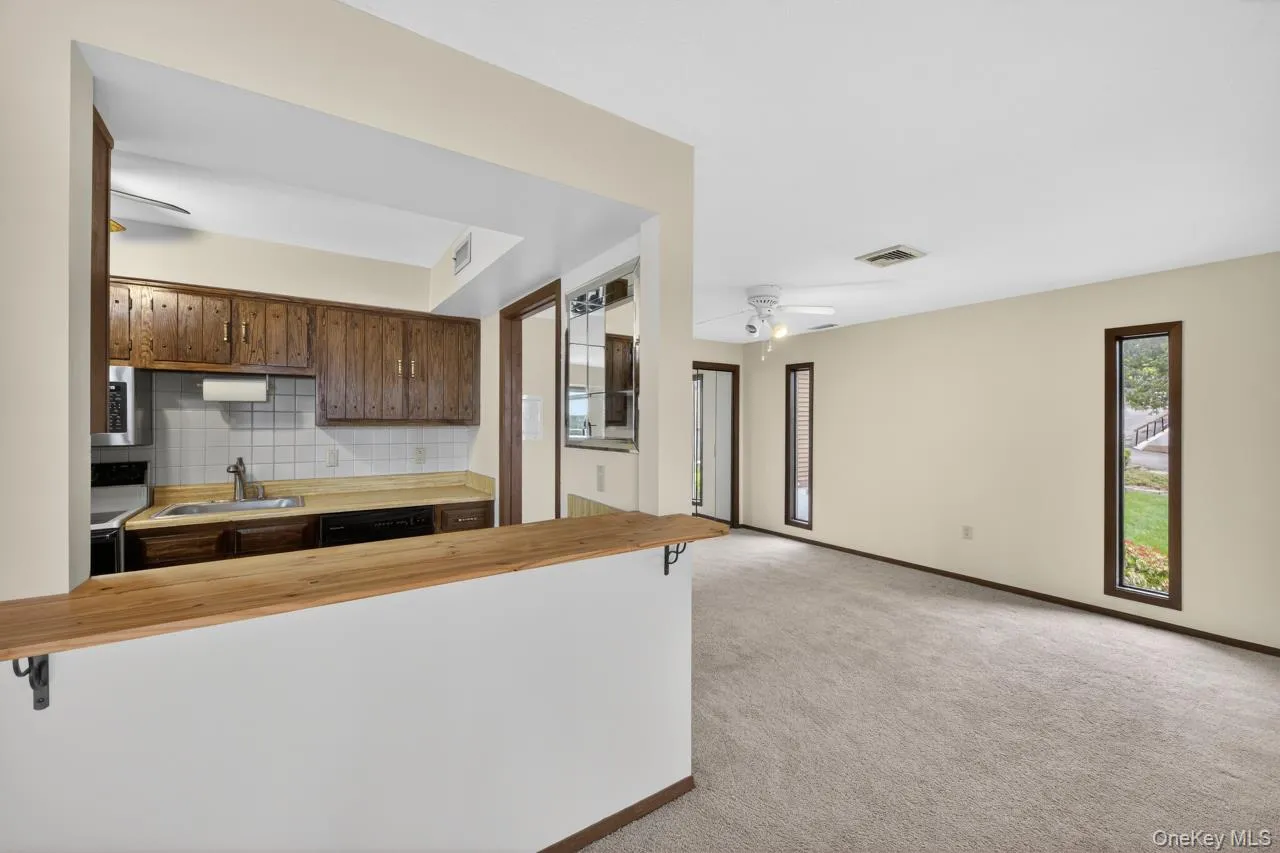 Kitchen pass-through with a wood-finish countertop, dark wood cabinetry, white tile backsplash, and stainless steel appliances Kitchen pass-through with a wood-finish countertop, dark wood cabinetry, white tile backsplash, and stainless steel appliances