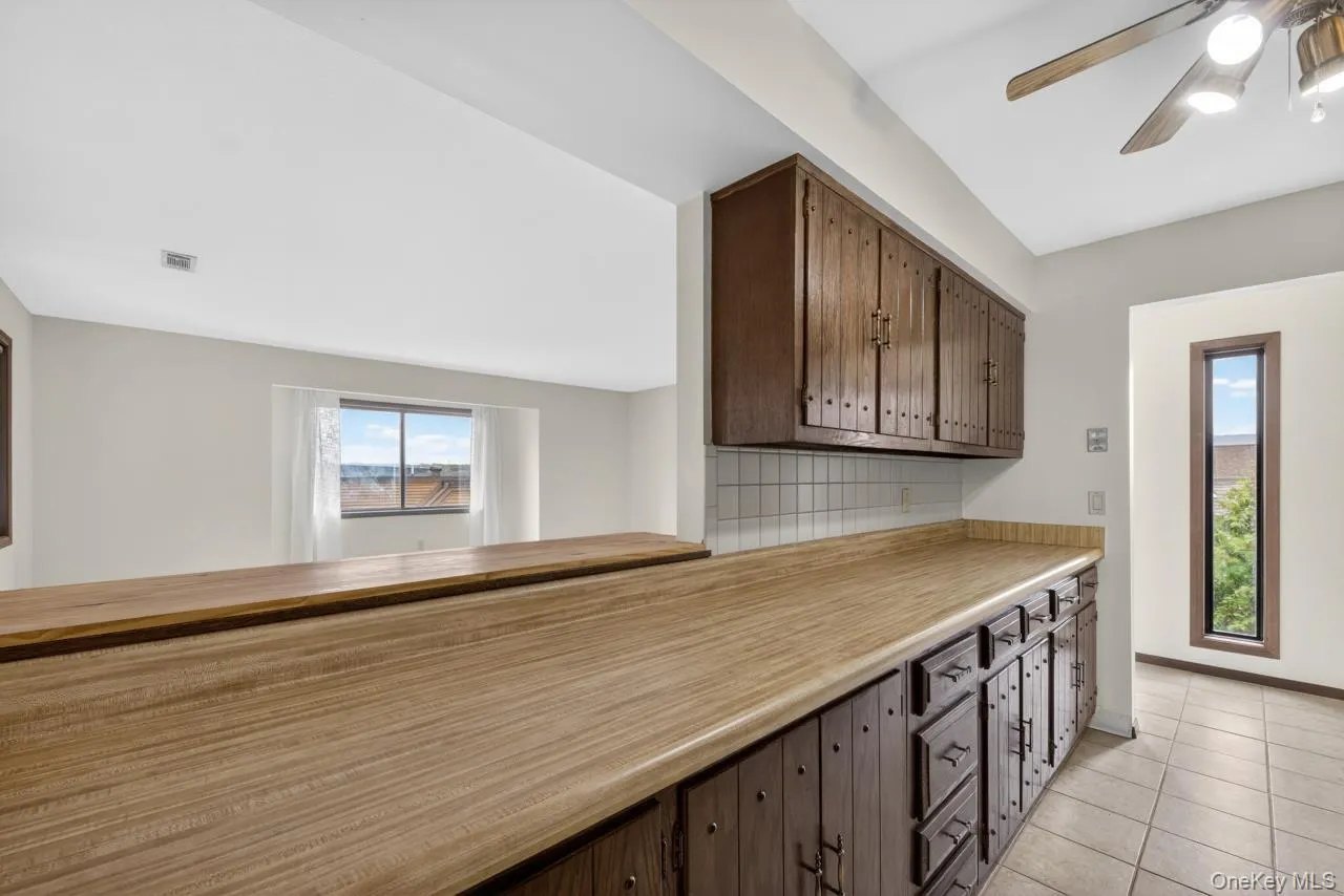 Kitchen featuring a wood-finish countertop, wood-finish cabinetry, a tiled backsplash, and tiled flooring Kitchen featuring a wood-finish countertop, wood-finish cabinetry, a tiled backsplash, and tiled flooring