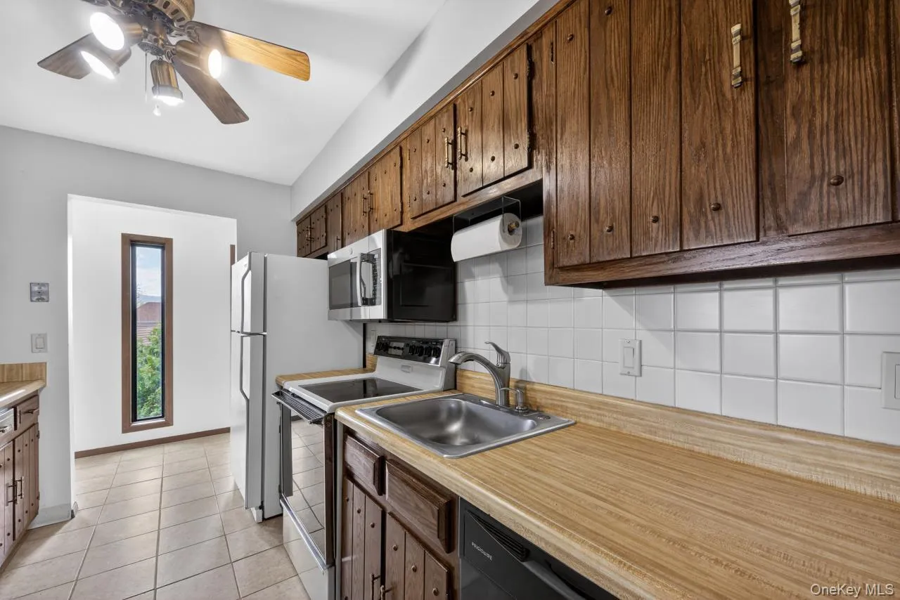 Kitchen with wood-finish cabinetry, tile flooring, and white square tile backsplash Kitchen with wood-finish cabinetry, tile flooring, and white square tile backsplash