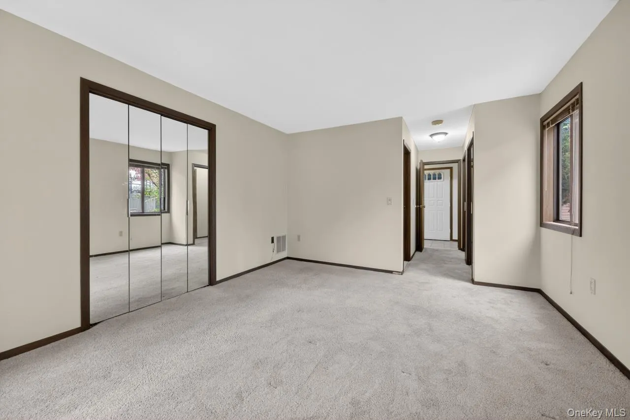 Carpeted interior space featuring a mirrored closet, a window with dark wood trim, light beige walls, and dark baseboards Carpeted interior space featuring a mirrored closet, a window with dark wood trim, light beige walls, and dark baseboards