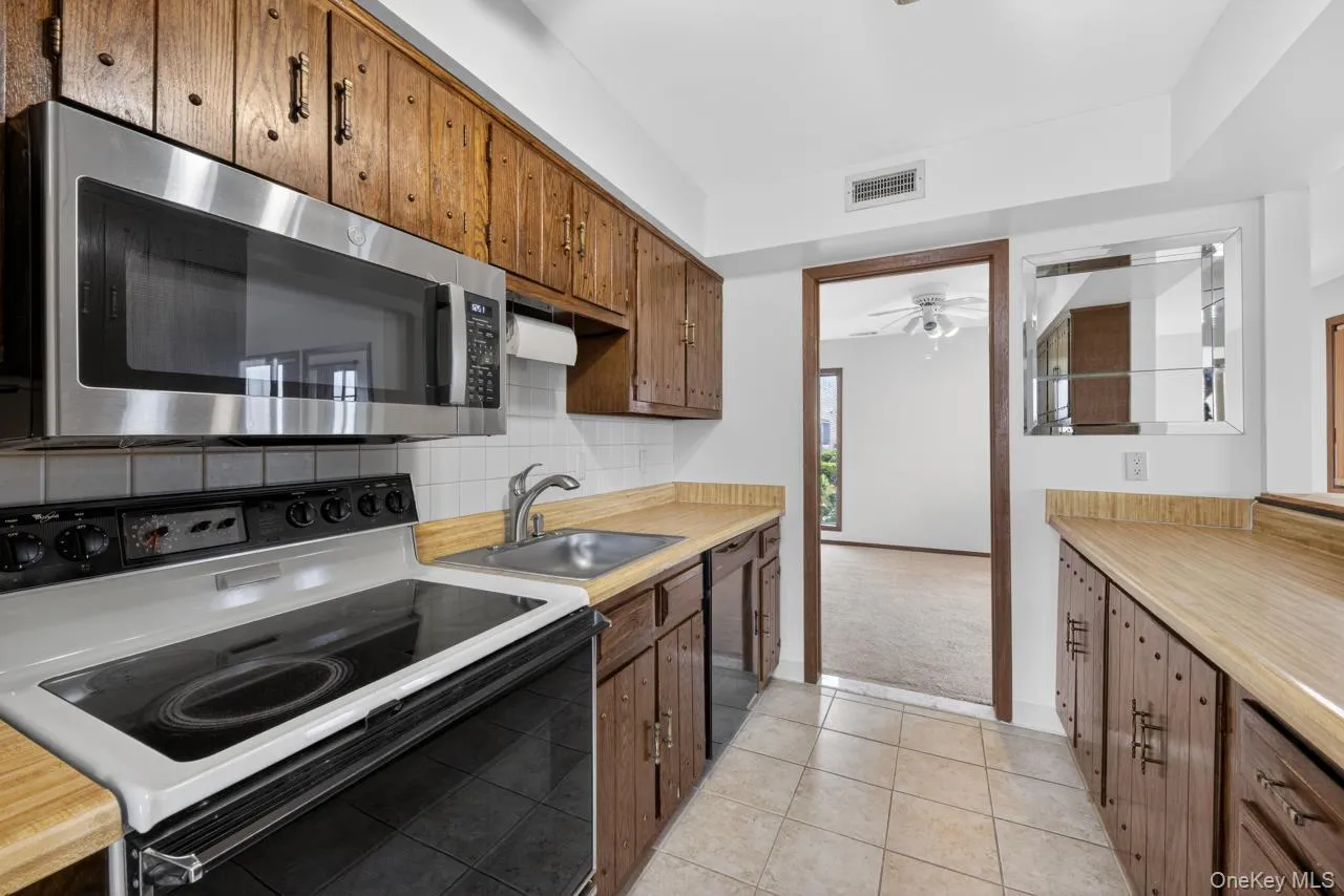 Kitchen featuring wood cabinetry, laminate countertops, a stainless steel over-the-range microwave, and a ceramic tile backsplash Kitchen featuring wood cabinetry, laminate countertops, a stainless steel over-the-range microwave, and a ceramic tile backsplash
