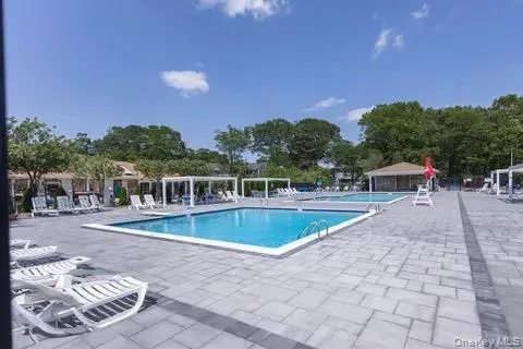 Outdoor swimming pool area featuring a large paved patio, lounge chairs, and a shaded pergola Outdoor swimming pool area featuring a large paved patio, lounge chairs, and a shaded pergola