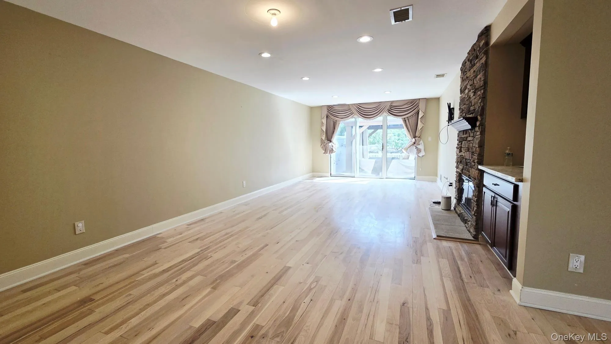 Open living area featuring hardwood floors, recessed lighting, and a stone fireplace Open living area featuring hardwood floors, recessed lighting, and a stone fireplace