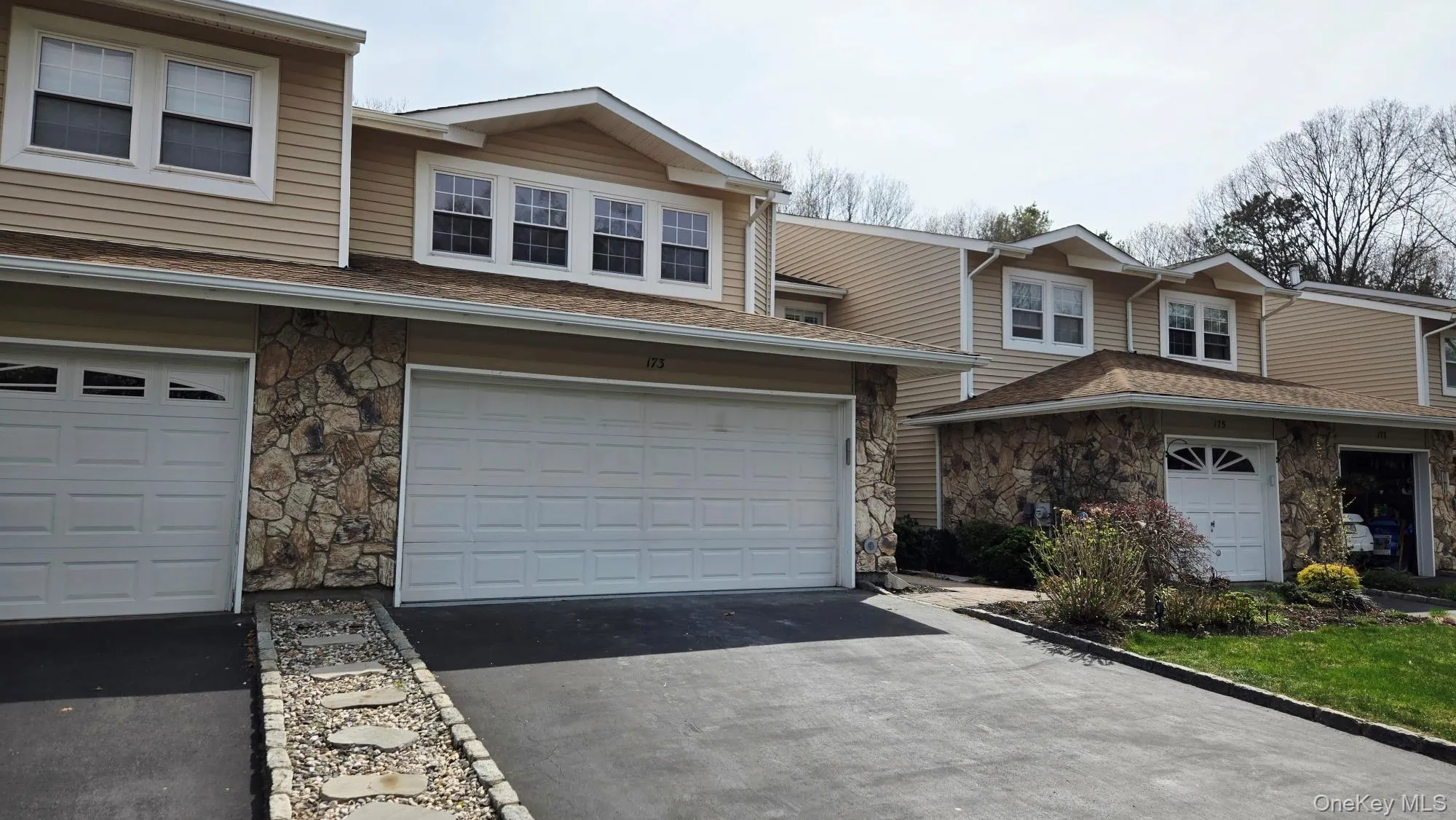 The property features a stone facade and siding exterior, with white garage doors and a paved driveway The property features a stone facade and siding exterior, with white garage doors and a paved driveway