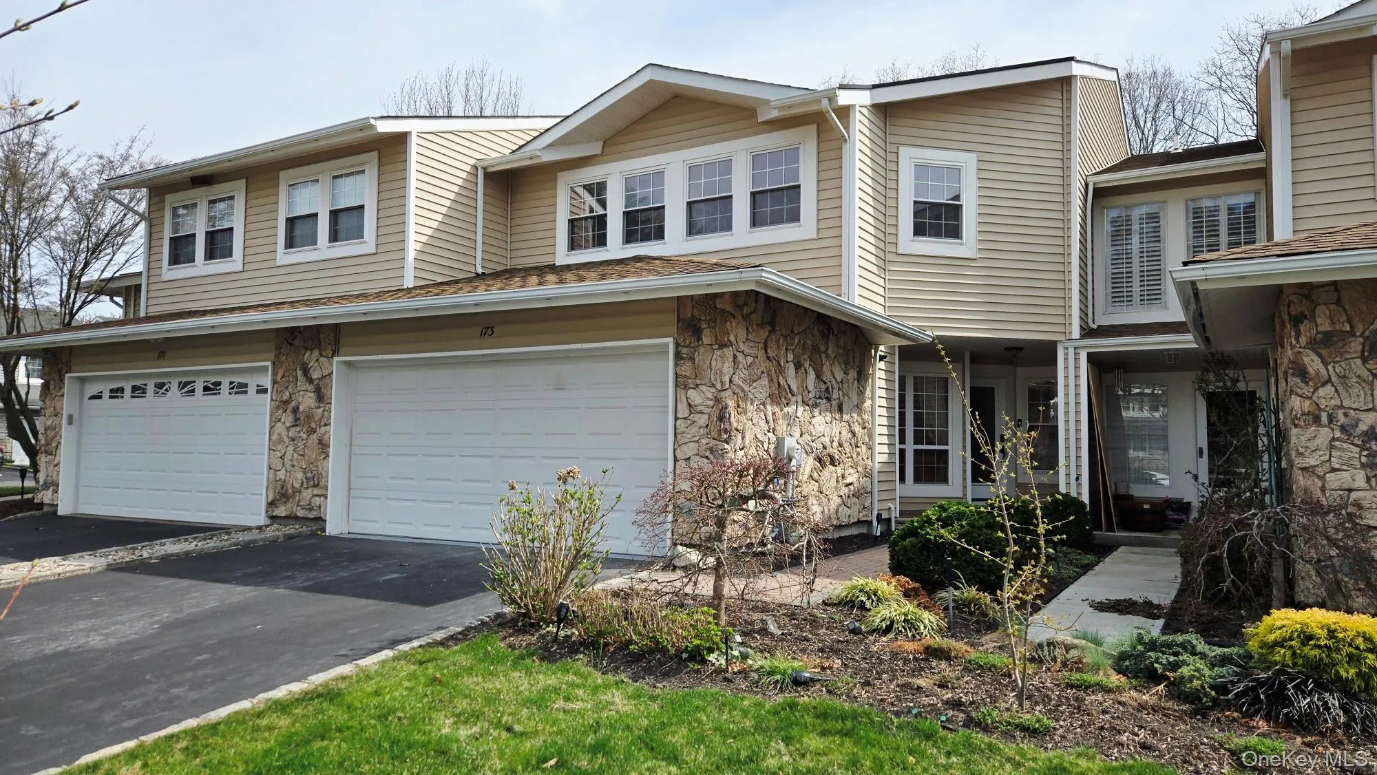 The property features a stone and siding facade, an attached garage, a paved driveway, and landscaping with mature plantings The property features a stone and siding facade, an attached garage, a paved driveway, and landscaping with mature plantings