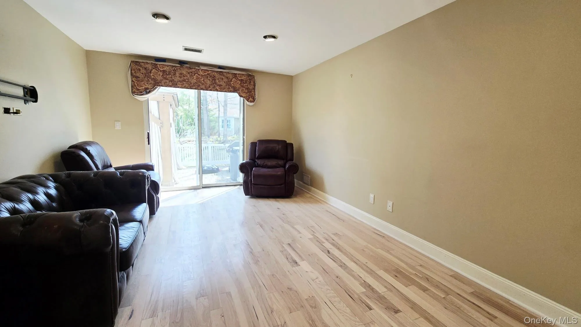 Bright living area featuring hardwood floors and a sliding glass door with a decorative valance, providing access to an outdoor deck Bright living area featuring hardwood floors and a sliding glass door with a decorative valance, providing access to an outdoor deck