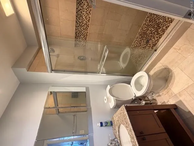 The bathroom features a vanity with a granite countertop and an integrated sink, a commode, and a shower with sliding glass doors The bathroom features a vanity with a granite countertop and an integrated sink, a commode, and a shower with sliding glass doors