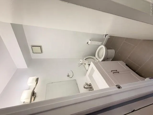 This bathroom features a white vanity with cabinet storage, a modern light fixture, and a wall-mounted mirror This bathroom features a white vanity with cabinet storage, a modern light fixture, and a wall-mounted mirror