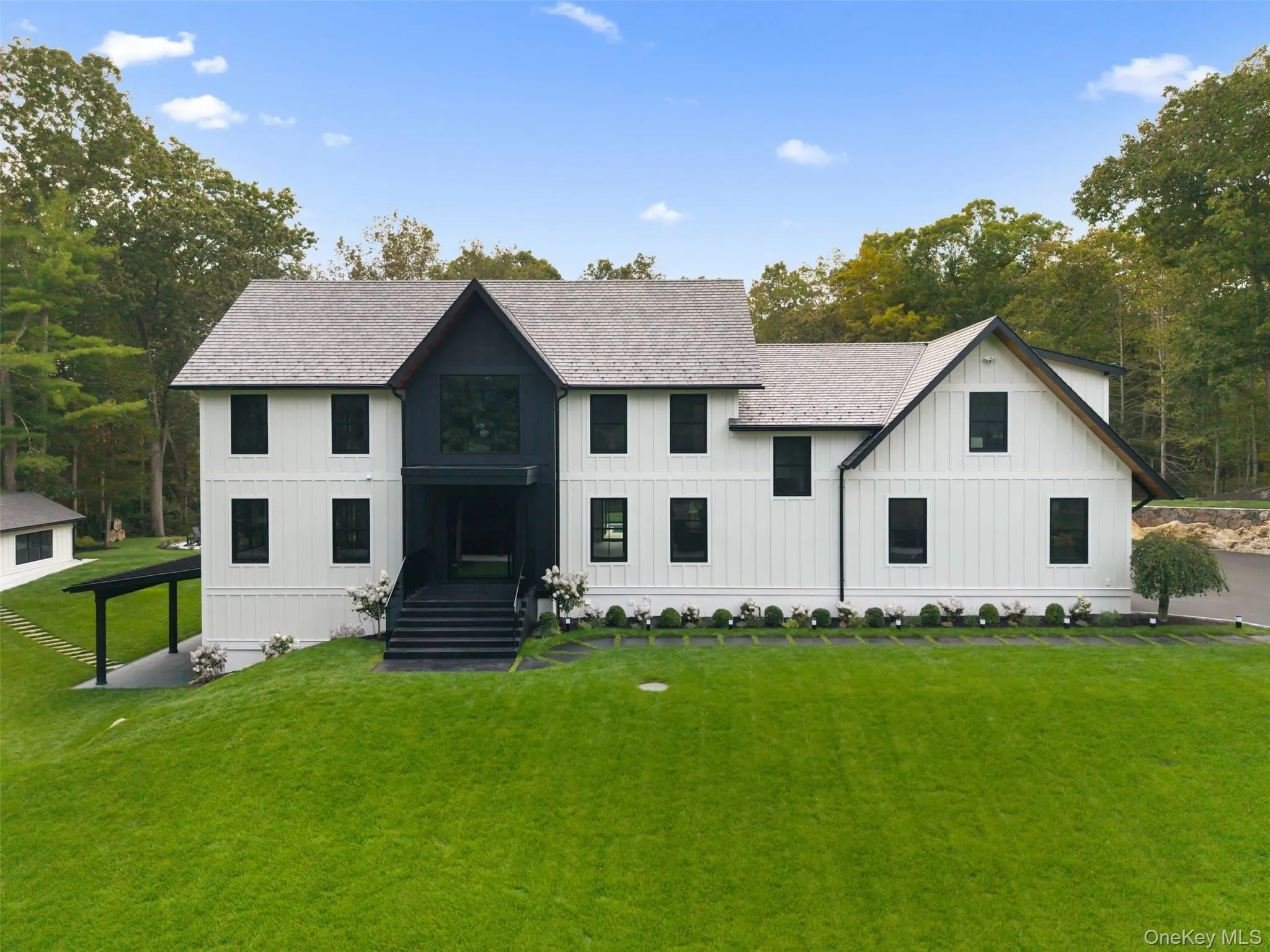 Modern inspired farmhouse with board and batten siding, a front yard, a shingled roof, and view of wooded area Modern inspired farmhouse with board and batten siding, a front yard, a shingled roof, and view of wooded area