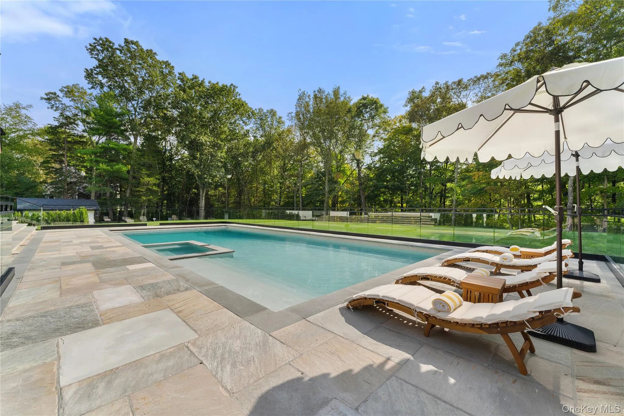 View of swimming pool featuring a patio, a pool with connected hot tub, and view of scattered trees View of swimming pool featuring a patio, a pool with connected hot tub, and view of scattered trees
