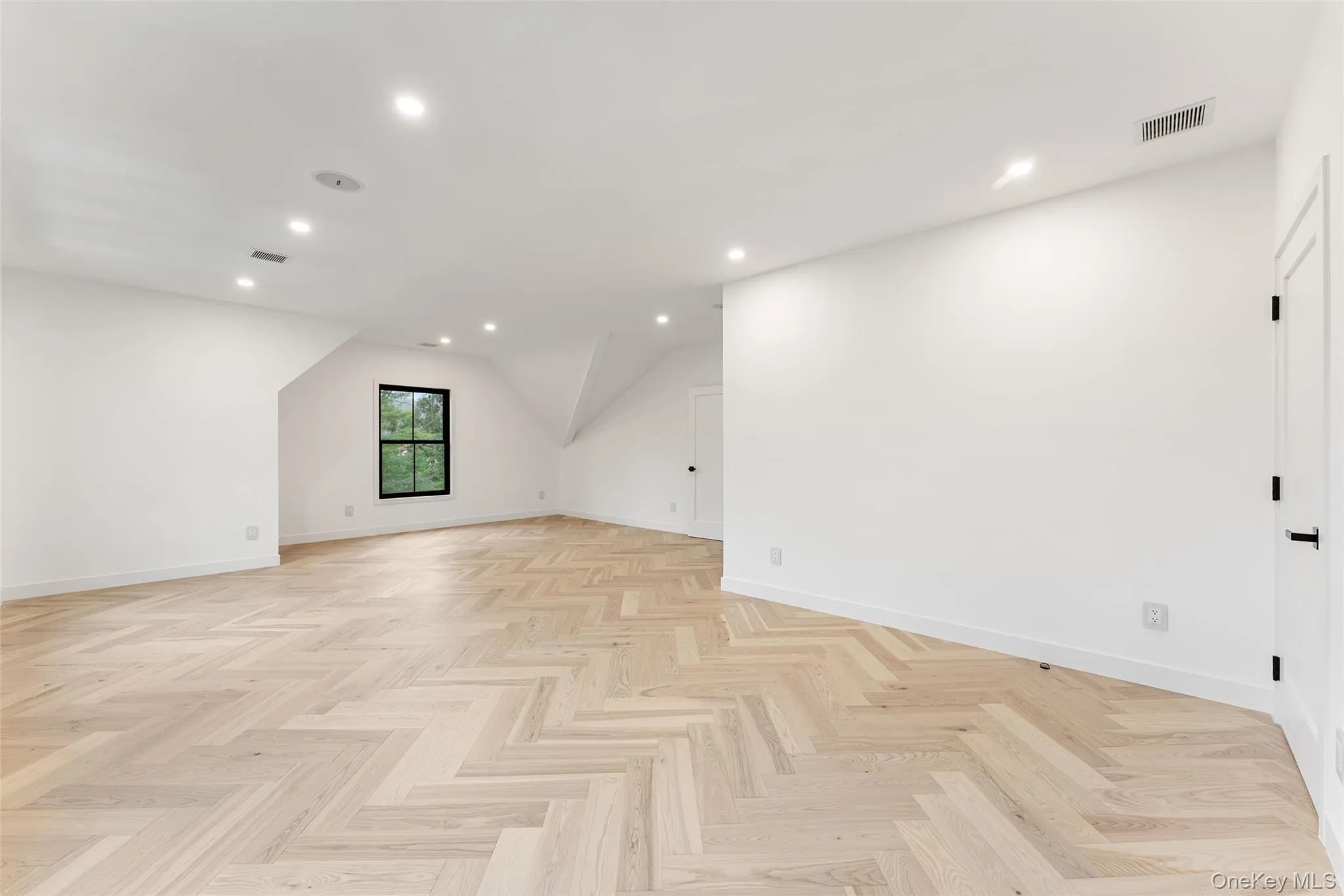 This versatile bedroom features light-toned hardwood flooring in a herringbone pattern, recessed lighting, and a window providing natural light This versatile bedroom features light-toned hardwood flooring in a herringbone pattern, recessed lighting, and a window providing natural light