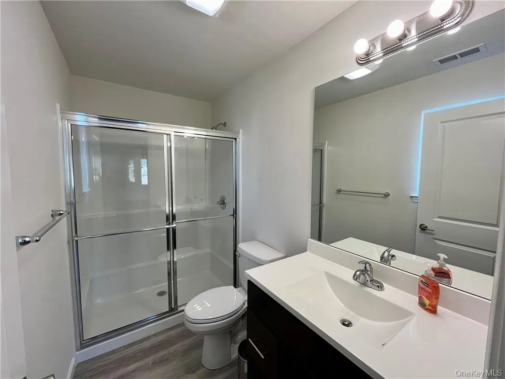 Bathroom with vanity, toilet, a shower with door, and hardwood / wood-style floors Bathroom with vanity, toilet, a shower with door, and hardwood / wood-style floors