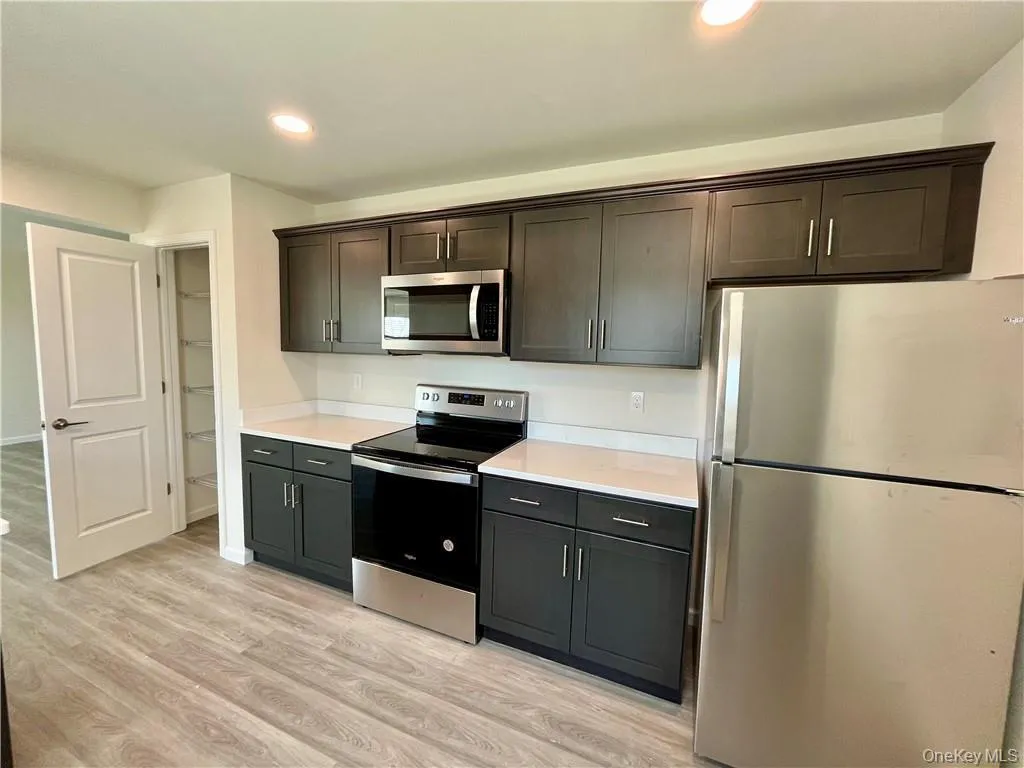 Kitchen featuring dark brown cabinetry, light wood-type flooring, and appliances with stainless steel finishes Kitchen featuring dark brown cabinetry, light wood-type flooring, and appliances with stainless steel finishes