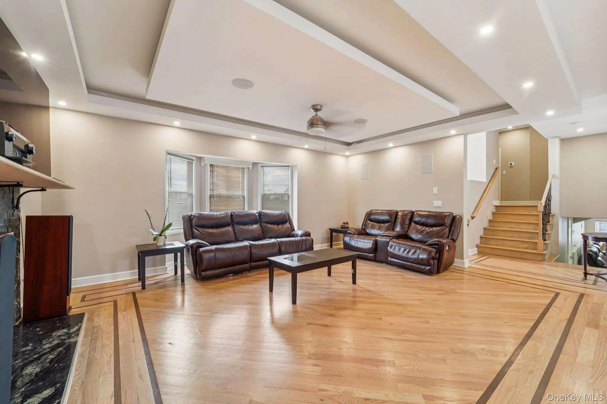 Spacious living area featuring hardwood flooring with decorative inlay, a bay window, and a tray ceiling with recessed lighting Spacious living area featuring hardwood flooring with decorative inlay, a bay window, and a tray ceiling with recessed lighting