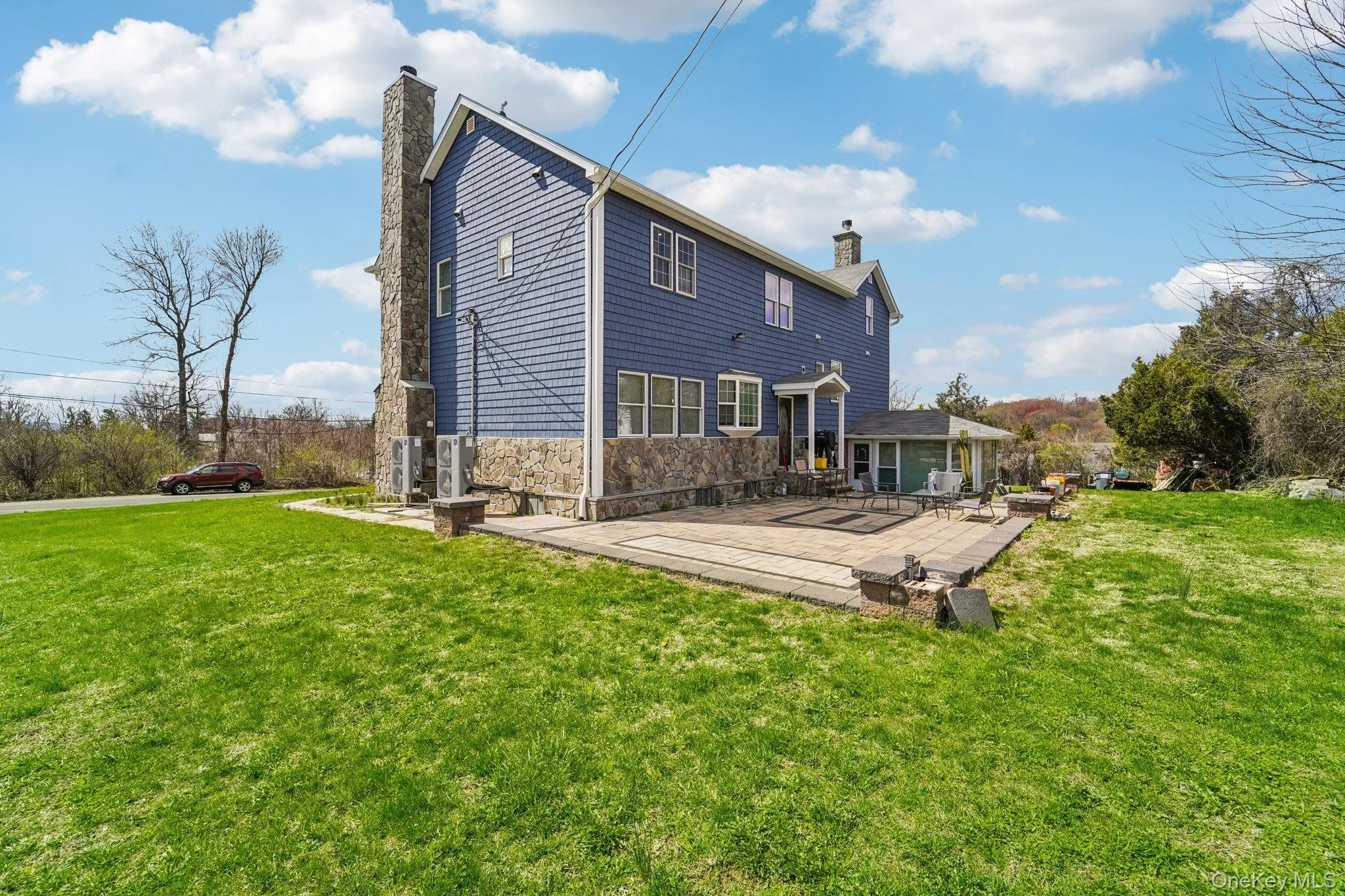 The property features blue siding, a stone foundation, and a stone paver patio with decorative darker stone accents. The property features blue siding, a stone foundation, and a stone paver patio with decorative darker stone accents.