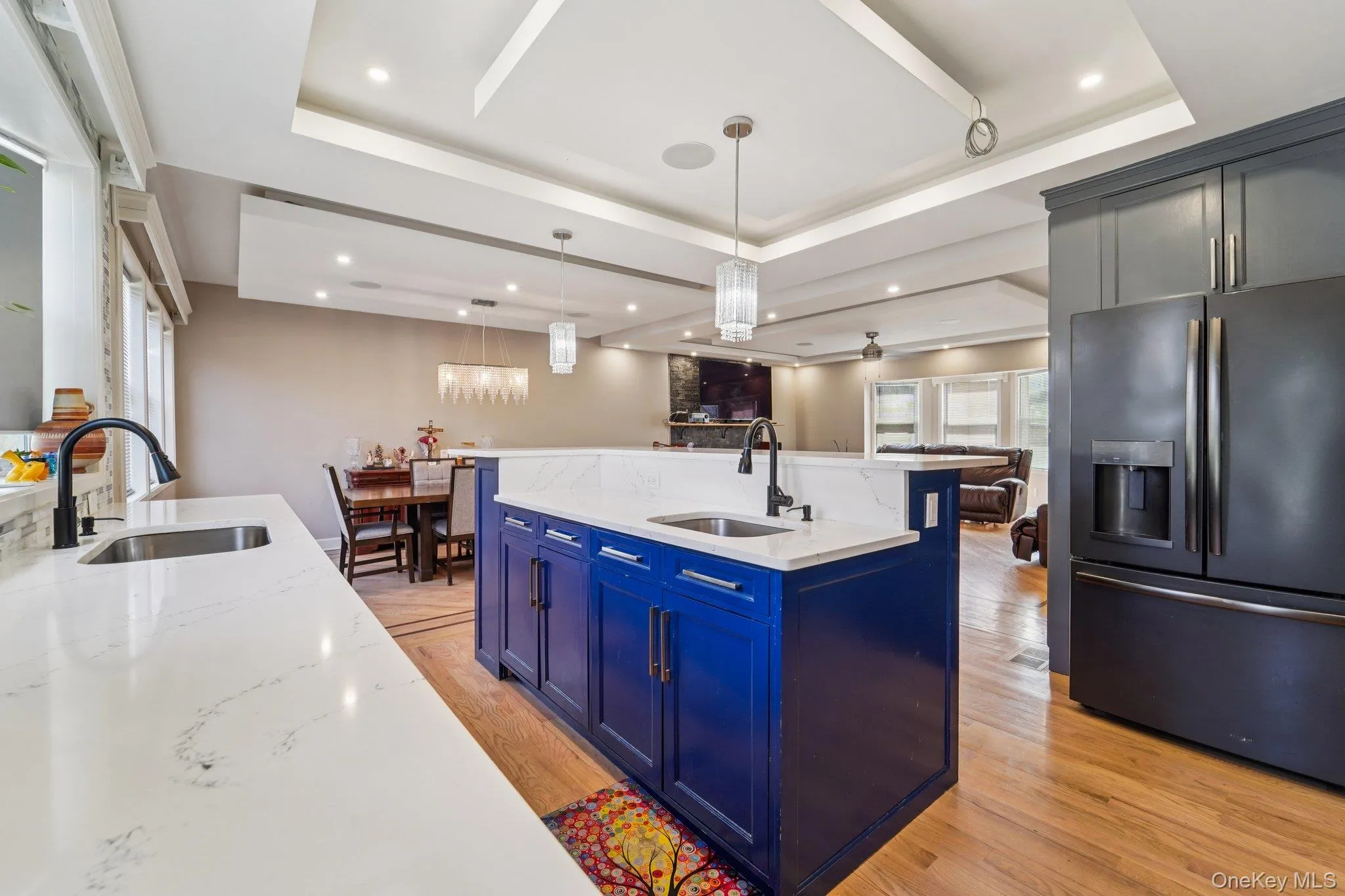 The open-concept kitchen features a blue island with seating, grey and blue cabinetry, and light countertops, complemented by a tiled backsplash. The open-concept kitchen features a blue island with seating, grey and blue cabinetry, and light countertops, complemented by a tiled backsplash.