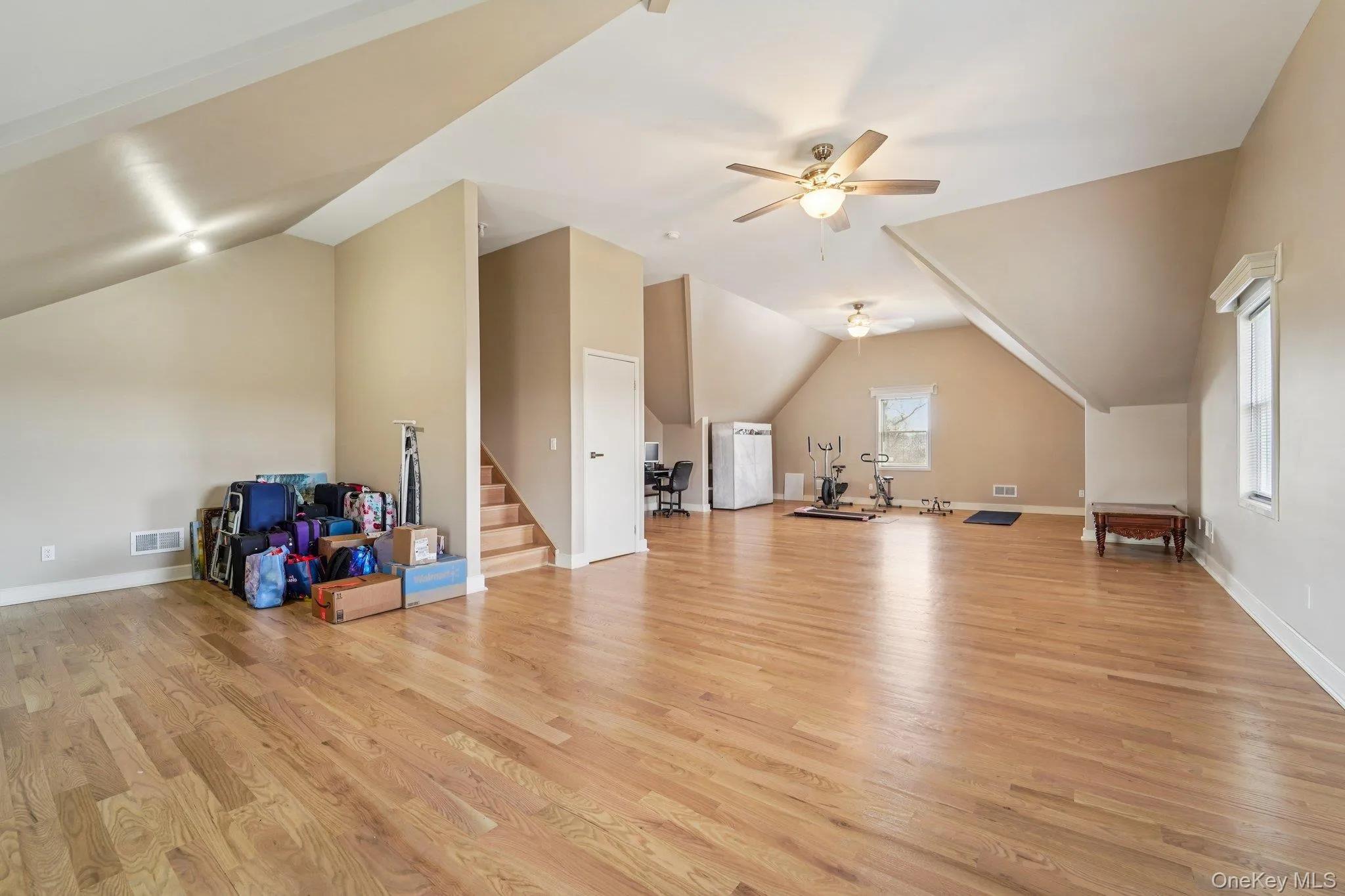 Expansive room featuring hardwood floors, sloped ceilings, and two ceiling fans for comfort. Expansive room featuring hardwood floors, sloped ceilings, and two ceiling fans for comfort.