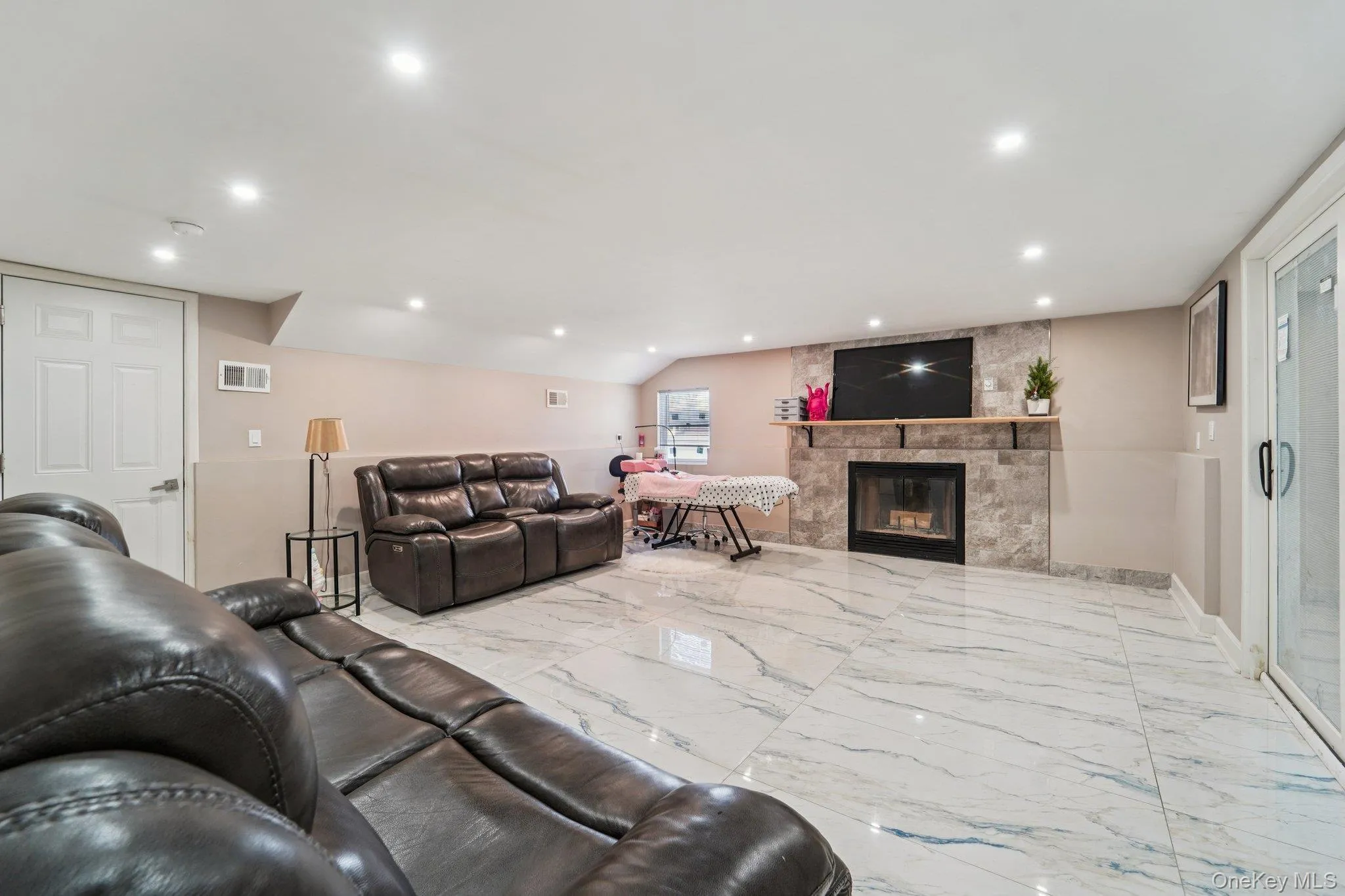 Spacious family room featuring large format marble-look tile flooring, a fireplace with a stone surround, and recessed lighting. Spacious family room featuring large format marble-look tile flooring, a fireplace with a stone surround, and recessed lighting.