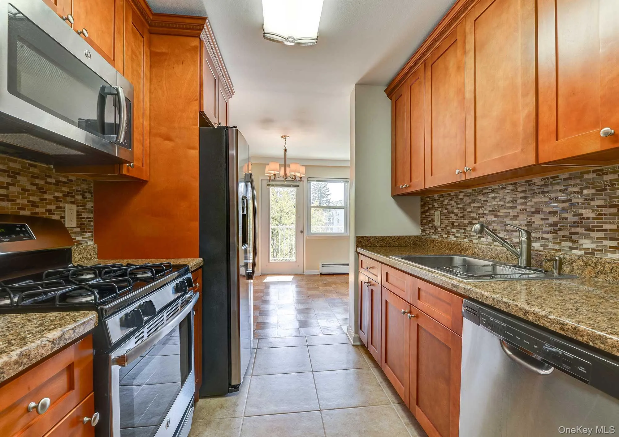 The kitchen features wood cabinetry, granite countertops, a tiled backsplash, and stainless steel appliances including a microwave, oven, and dishwasher The kitchen features wood cabinetry, granite countertops, a tiled backsplash, and stainless steel appliances including a microwave, oven, and dishwasher