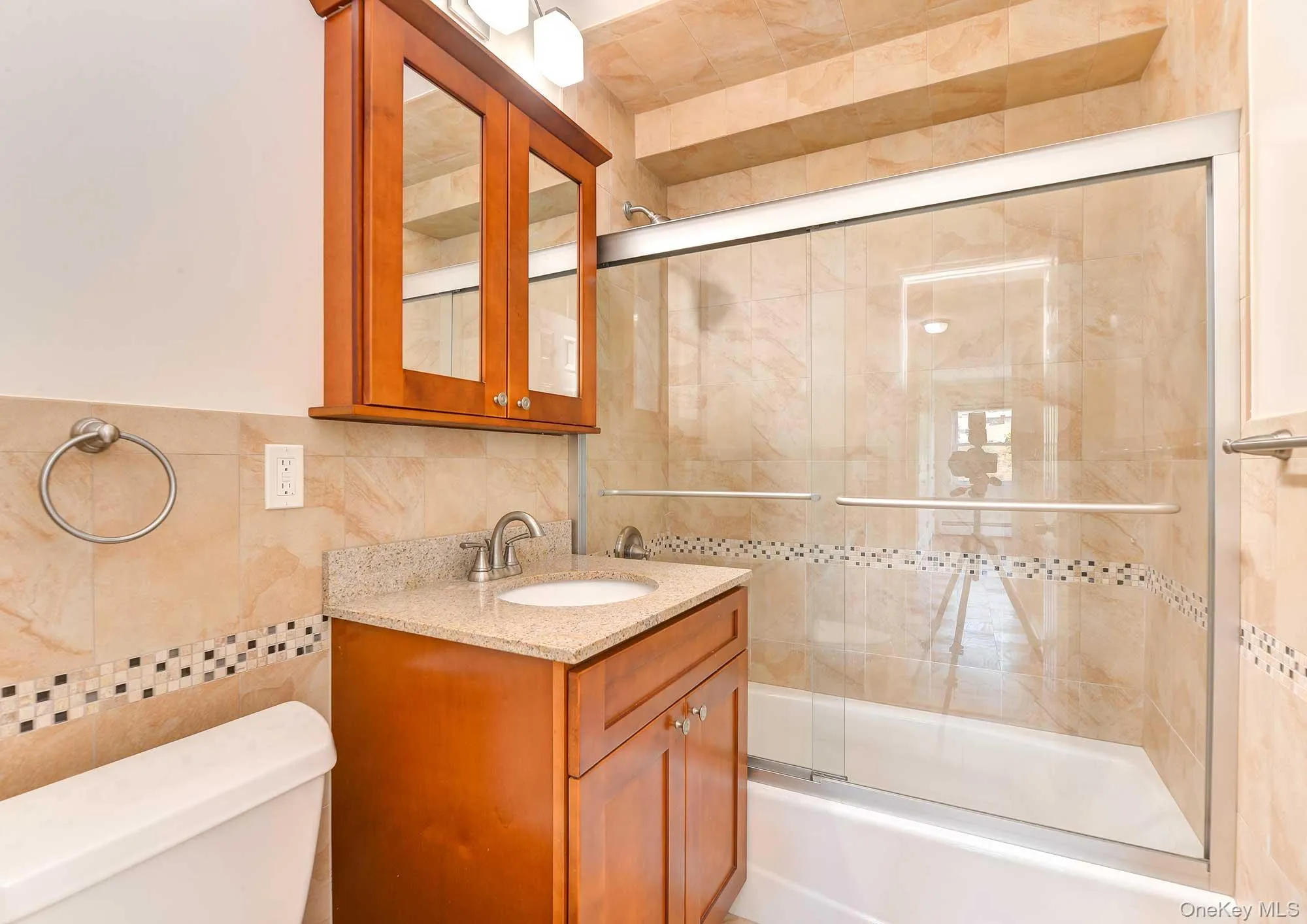 Bathroom featuring a vanity with a light-colored countertop, a medicine cabinet with mirrored doors, and a shower-tub combination with sliding glass doors Bathroom featuring a vanity with a light-colored countertop, a medicine cabinet with mirrored doors, and a shower-tub combination with sliding glass doors