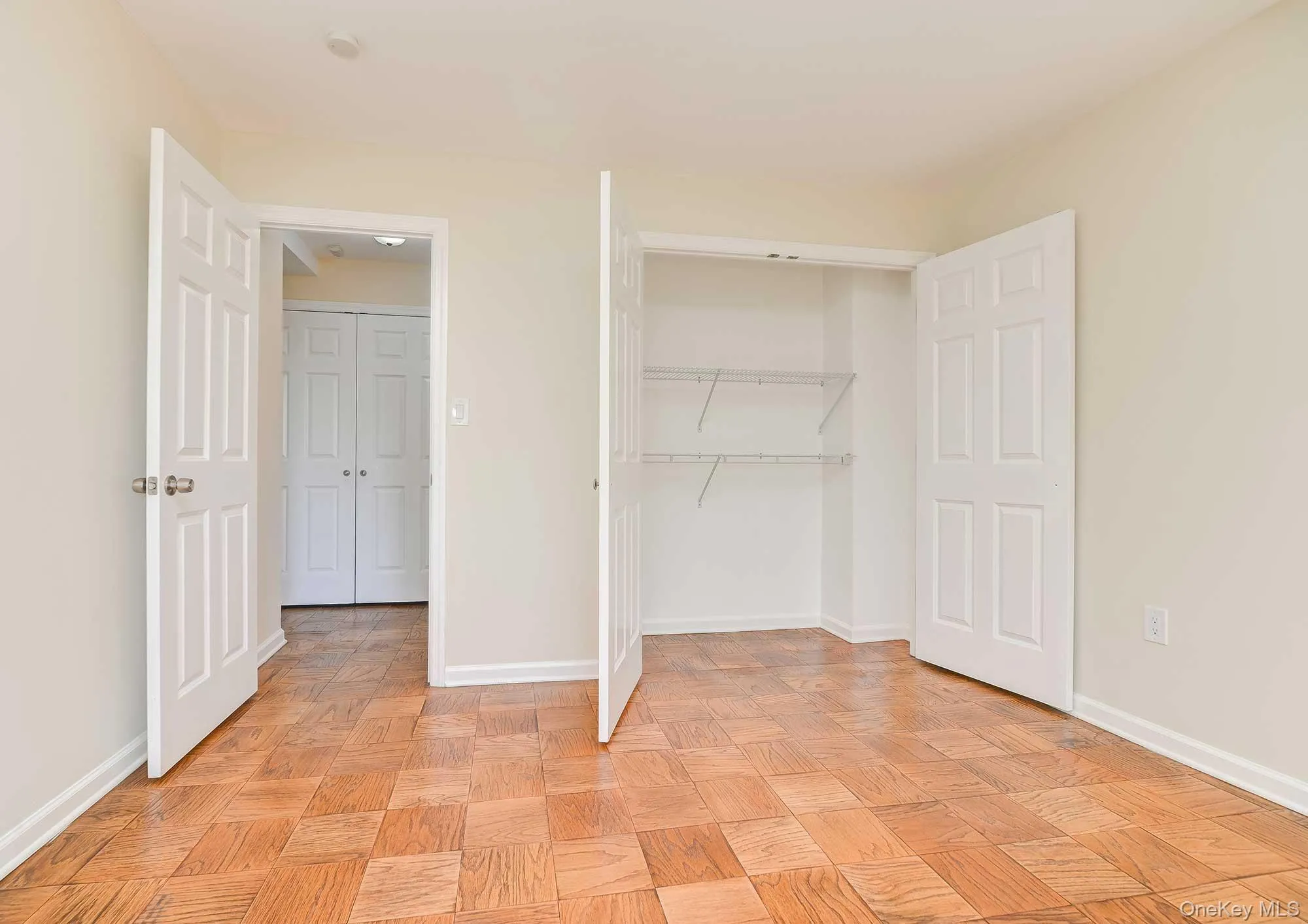 The room features parquet flooring, light-colored walls, and a built-in closet with shelving The room features parquet flooring, light-colored walls, and a built-in closet with shelving