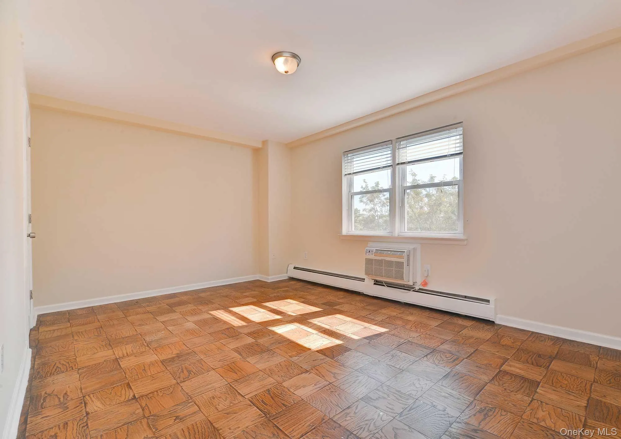 Spacious room featuring patterned wood flooring, a window providing natural light, and a window-mounted air conditioning unit Spacious room featuring patterned wood flooring, a window providing natural light, and a window-mounted air conditioning unit
