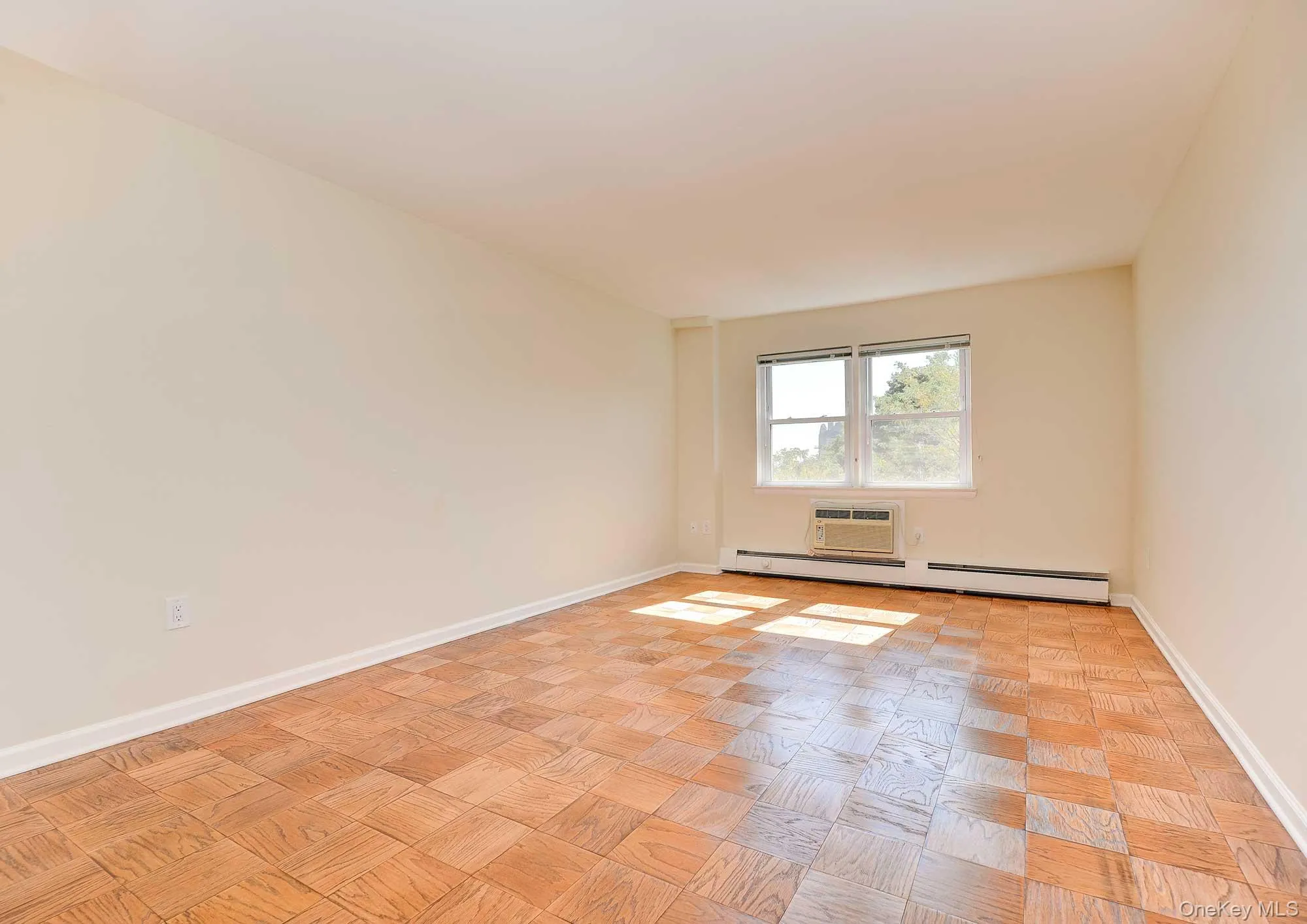 This space features parquet wood flooring, neutral colored walls, and a window with an air conditioning unit below it, offering natural light This space features parquet wood flooring, neutral colored walls, and a window with an air conditioning unit below it, offering natural light