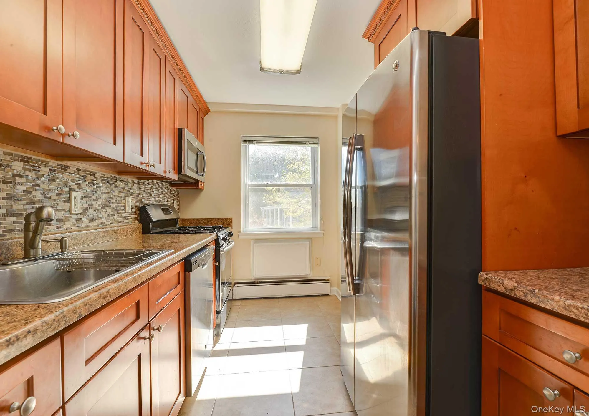 The kitchen features wood cabinetry, a mosaic tile backsplash, and stainless steel appliances including a refrigerator, microwave, and range The kitchen features wood cabinetry, a mosaic tile backsplash, and stainless steel appliances including a refrigerator, microwave, and range