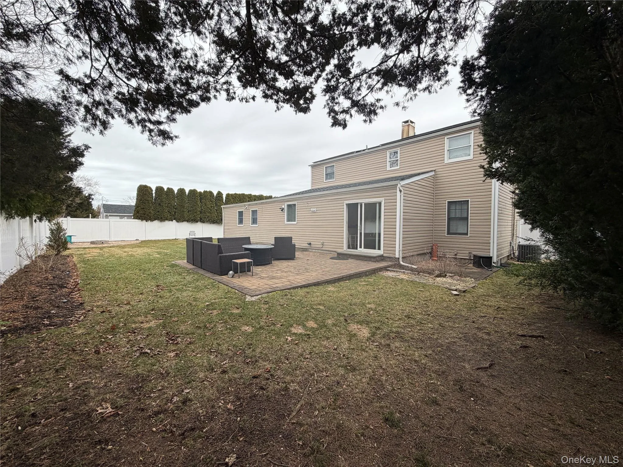 The property features a spacious rear yard with a lawn, a white fence, and a paved patio area The property features a spacious rear yard with a lawn, a white fence, and a paved patio area